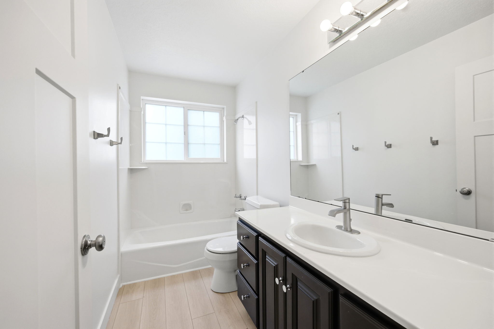 Bathroom featuring a white bathtub with a window, dark wood-finish vanity with white countertop, and wood-finish flooring