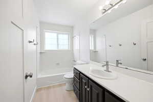 Bathroom featuring a white bathtub with a window, dark wood-finish vanity with white countertop, and wood-finish flooring