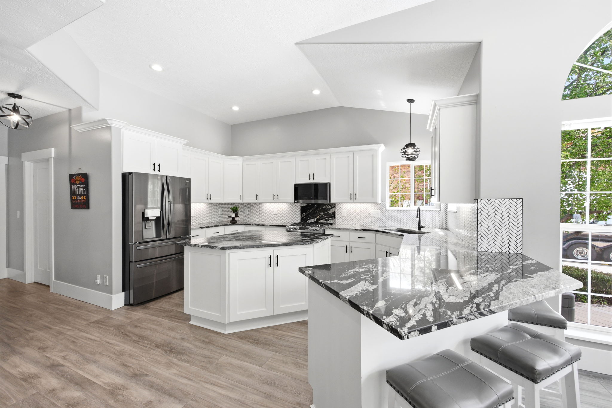Spacious kitchen featuring white cabinetry, dark stone countertops, stainless steel refrigerator, white subway tile backsplash, and wood-finish flooring