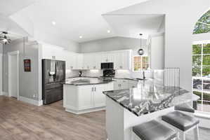 Spacious kitchen featuring white cabinetry, dark stone countertops, stainless steel refrigerator, white subway tile backsplash, and wood-finish flooring