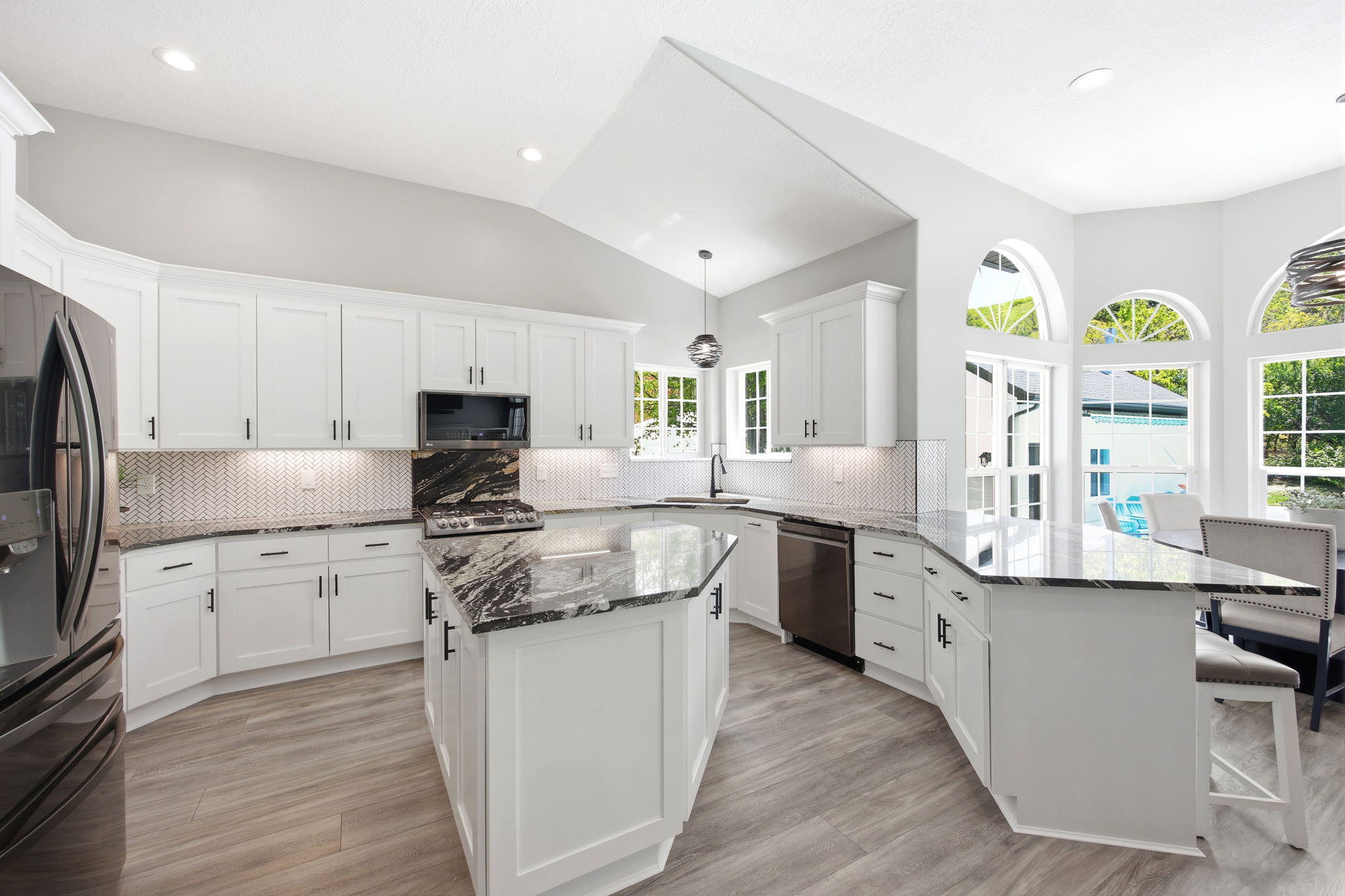 Bright kitchen featuring white cabinetry, black stone countertops, a central island, stainless steel appliances, and wood-finish flooring