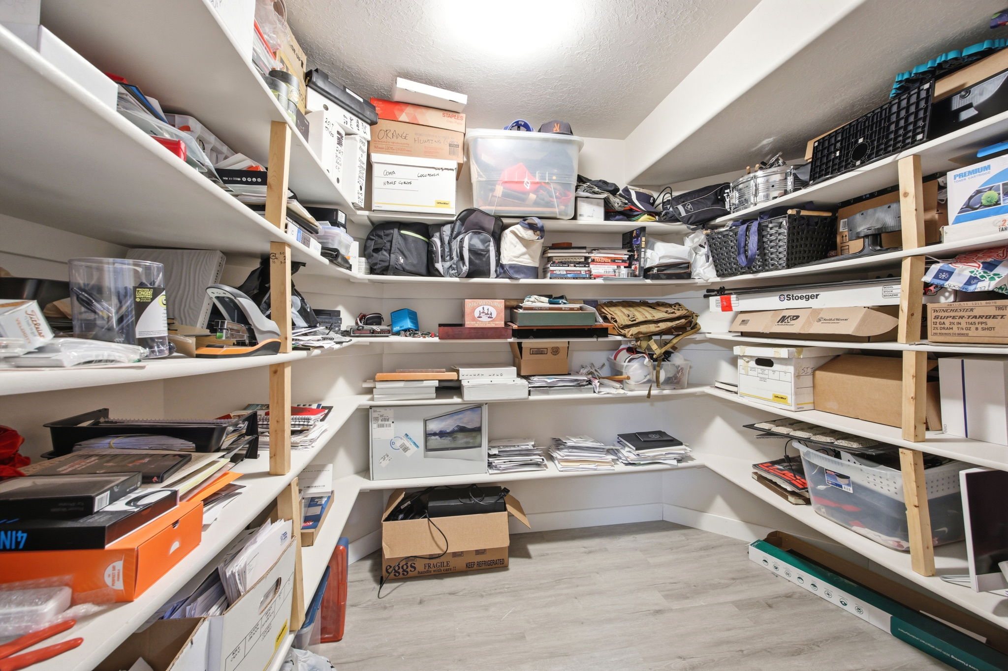 Spacious storage room featuring extensive built-in shelving, durable wood-finish flooring, and bright overhead lighting