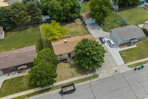 Aerial perspective showcasing the property with a light brown shingle roof, a light-colored exterior, and mature trees providing shade