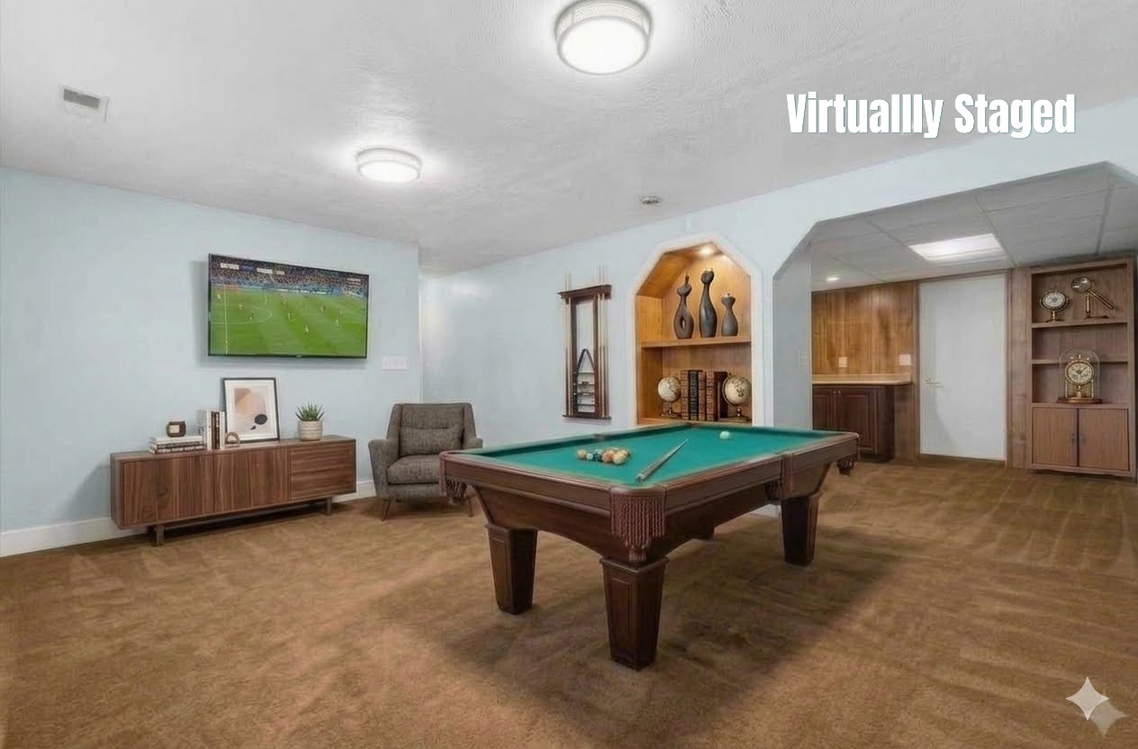 Spacious recreation room featuring recessed built-in shelving, a built-in wet bar with wood-finish cabinetry, light blue wall paint, and brown carpet flooring