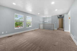 Spacious room with plush carpeting, two large windows with blinds, recessed lighting, and a partial baluster railing