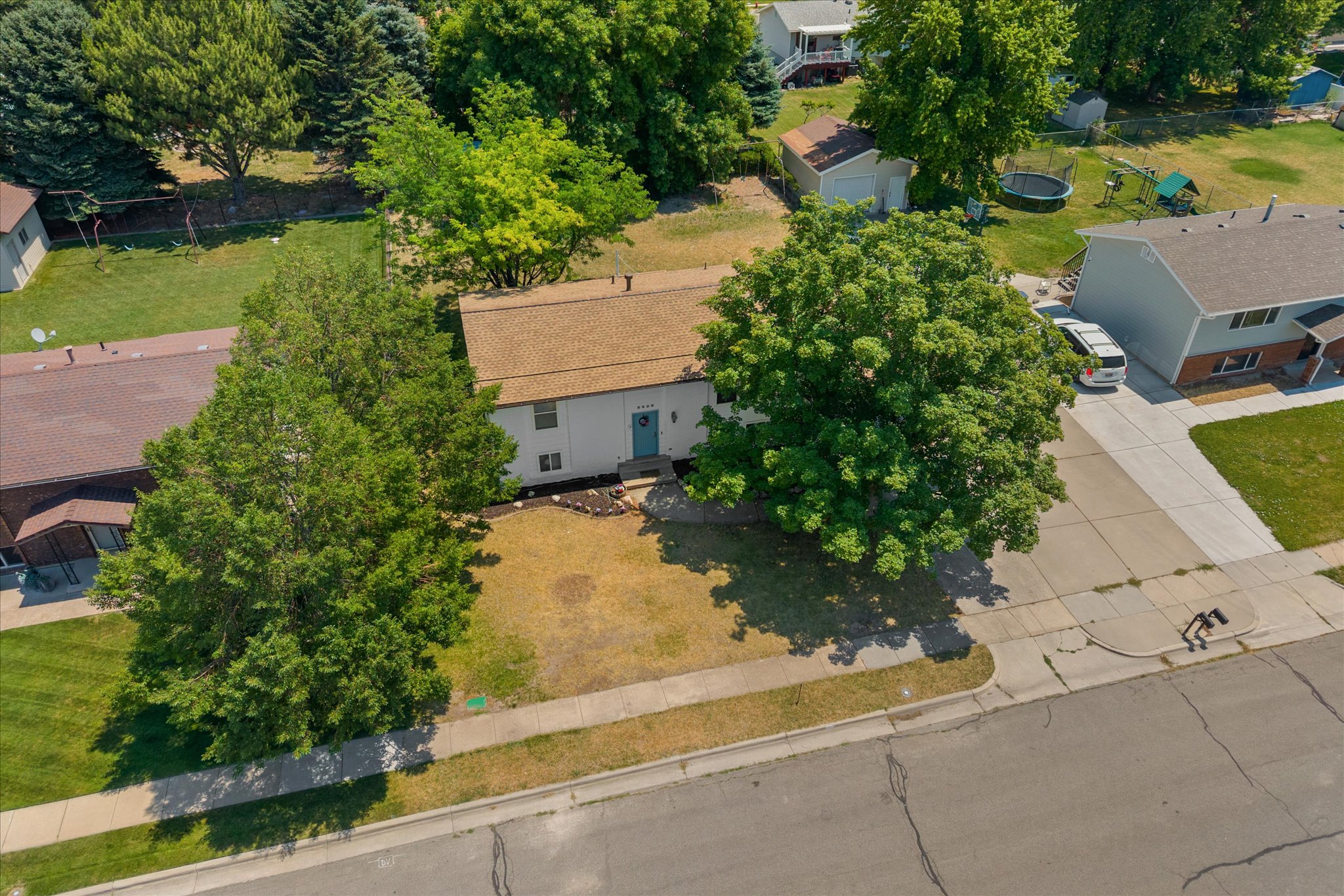 Split-level residence featuring a light-colored exterior, an attached garage, and mature trees in the front yard