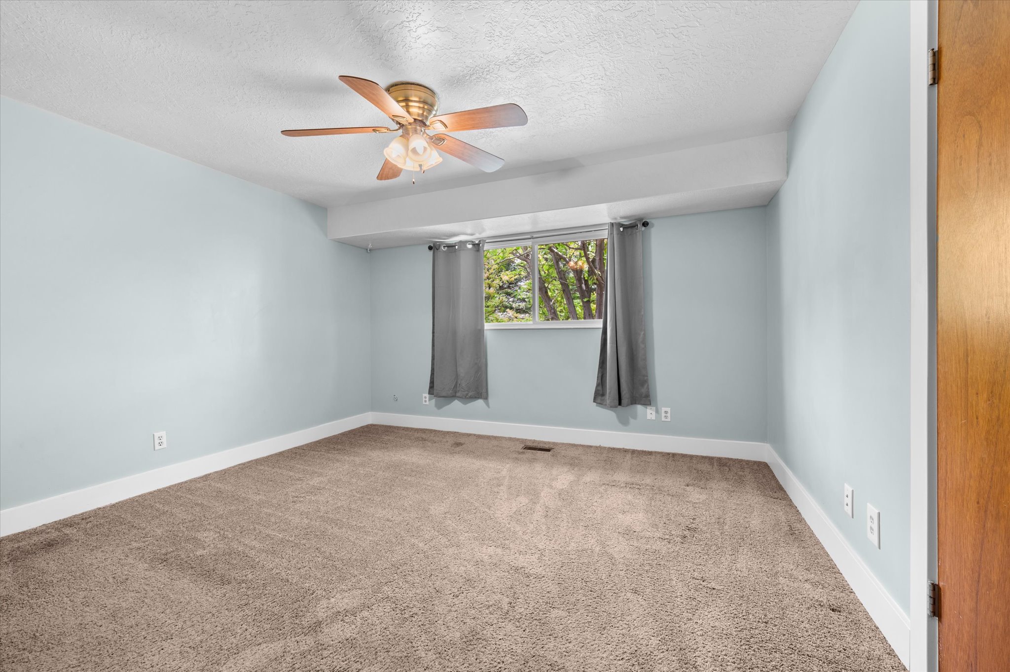 Carpeted Primary bedroom featuring a ceiling fan, a window with exterior tree scenery, and a bathroom entrance door.