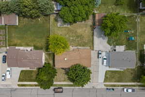 Aerial perspective showcasing a residential property with a brown shingle roof, a paved driveway, and a large green lawn