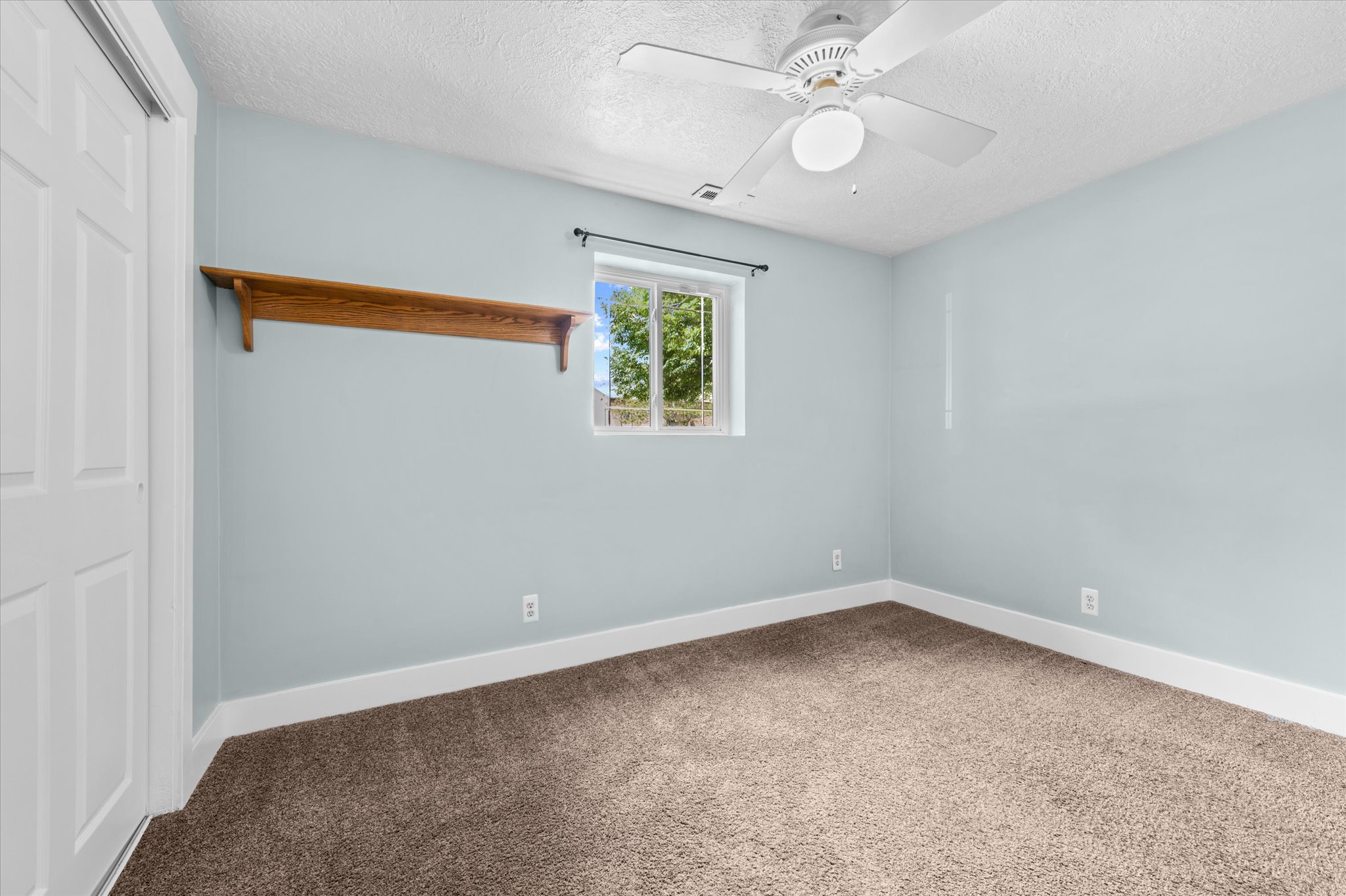 Bedroom #4 with Light blue interior wall, window with exterior landscape, built-in wooden shelf, and a ceiling fan with light fixture