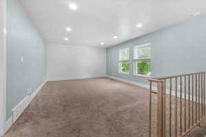 Spacious room featuring neutral carpeting, light blue painted walls, recessed lighting, and two windows with blinds