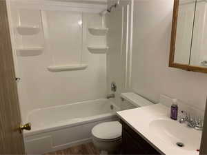 Bathroom featuring a white bathtub and shower combination with integrated shelving, a white single-sink vanity with a dark wood-finish cabinet, and wood-finish flooring