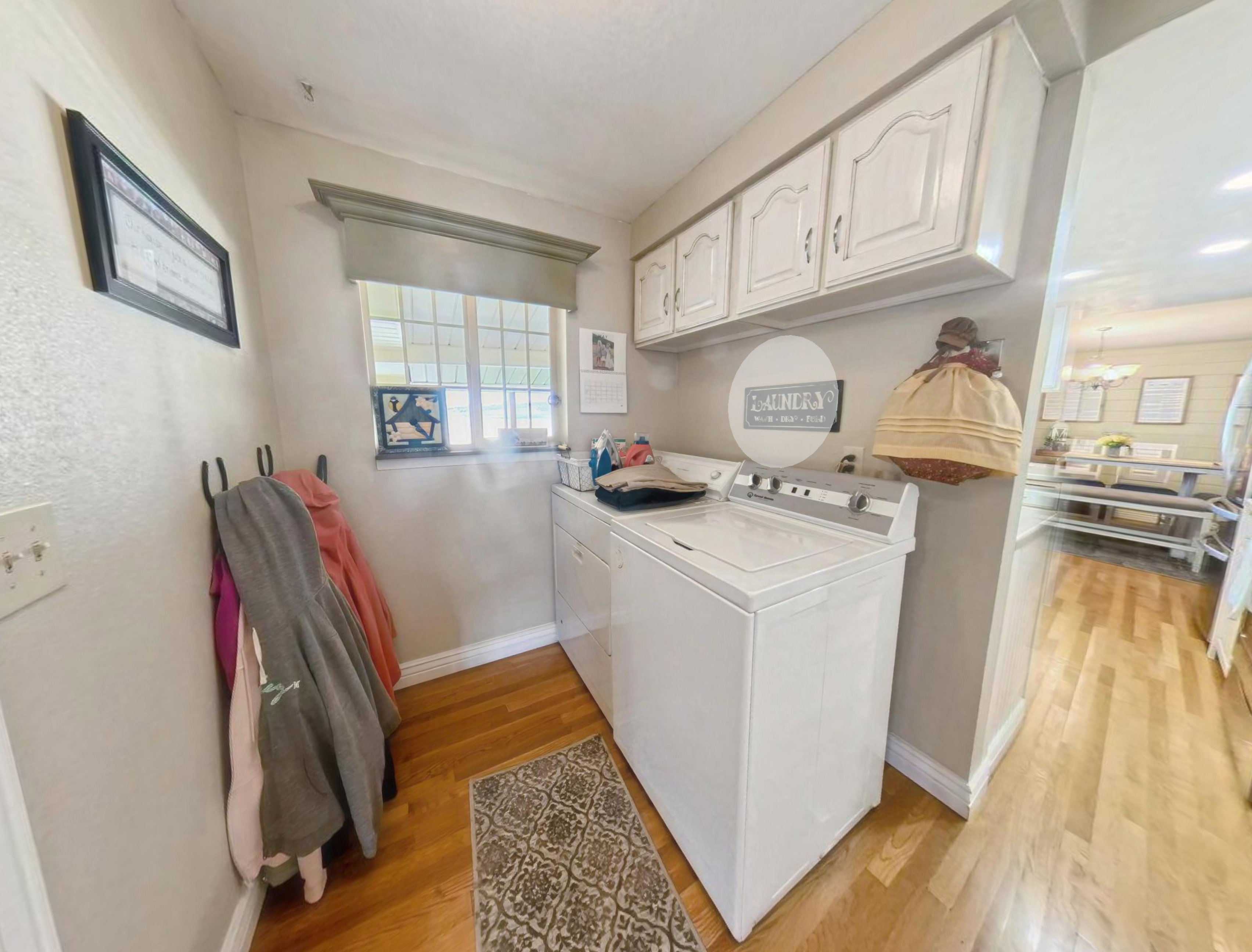 Dedicated utility space featuring light wood-finish flooring, white upper cabinetry, and a window with natural light