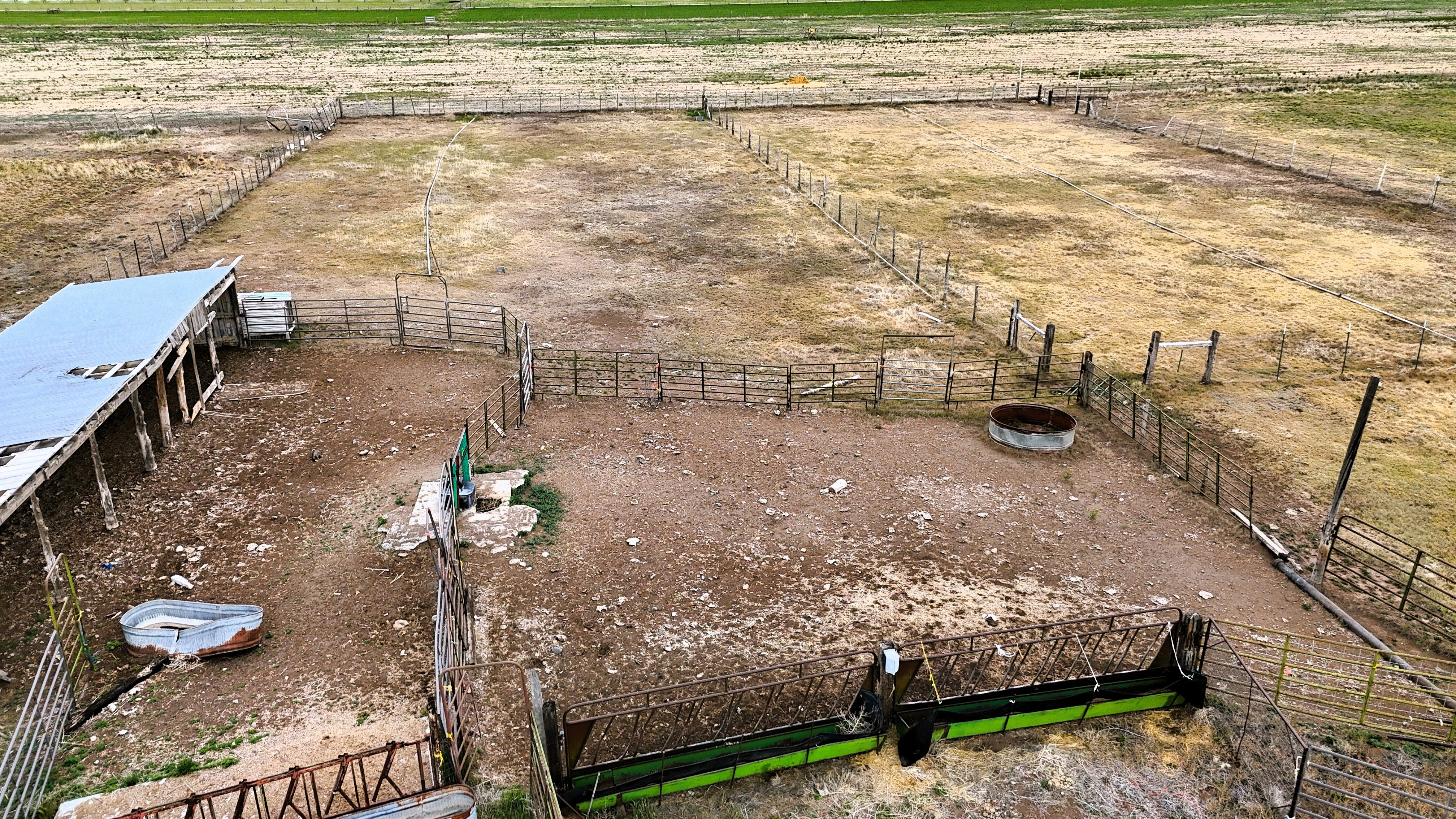 Fenced agricultural property featuring multiple pens, a metal-roofed shelter, and feeding troughs