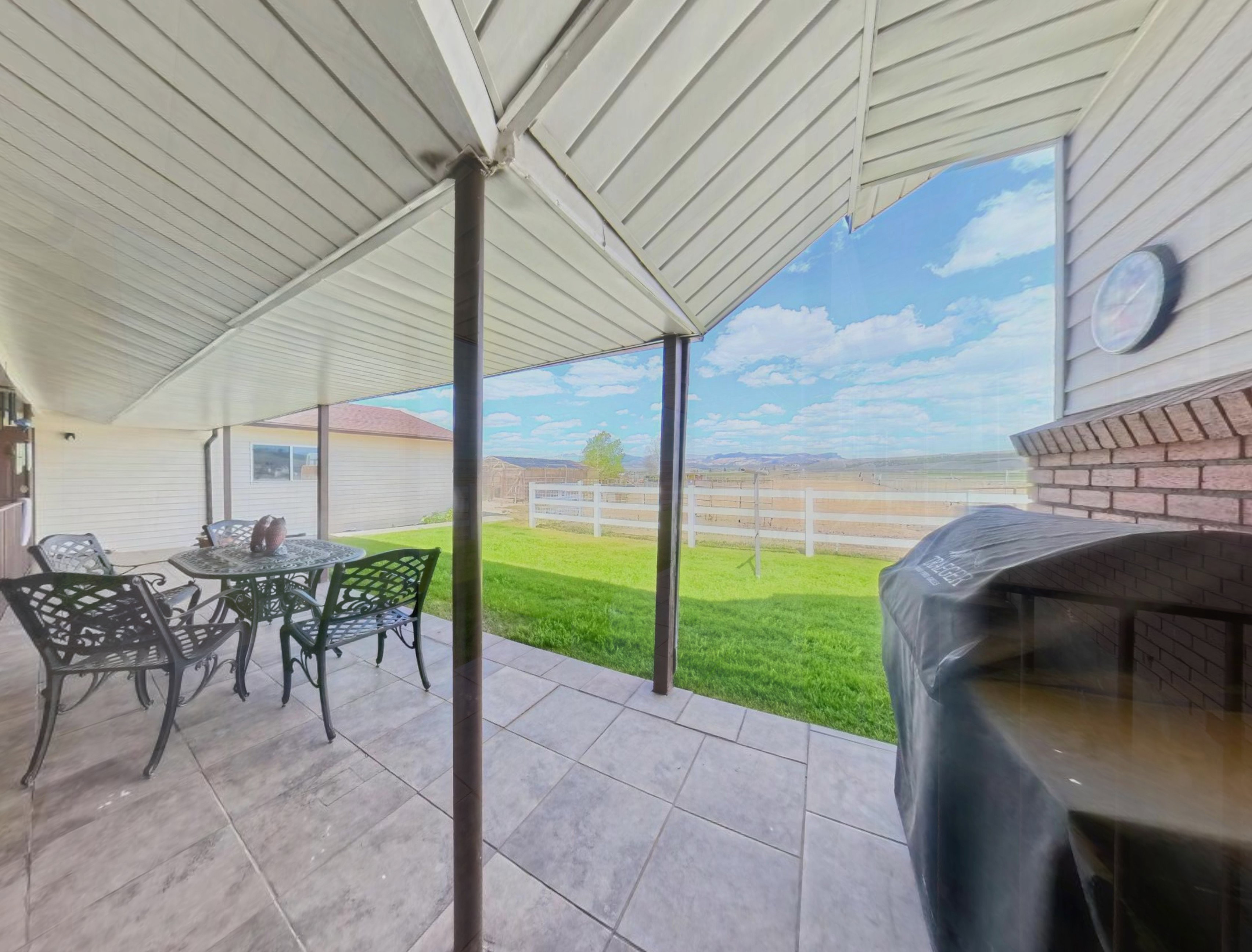 Covered patio featuring large format tile flooring, a white vinyl fence, and a backdrop of open terrain