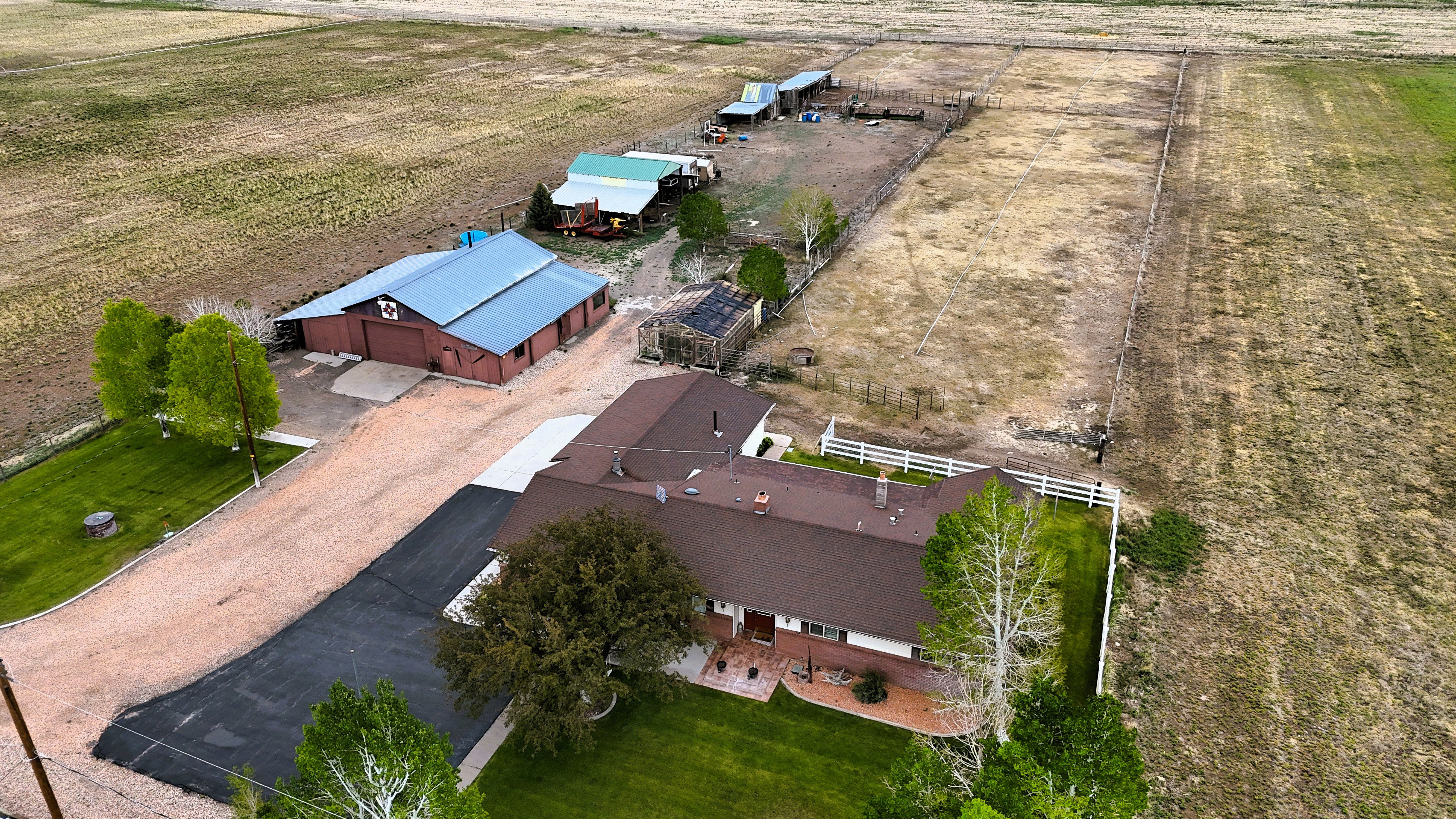Expansive property featuring a main residence with a brown shingle roof, asphalt driveway, and gravel parking area