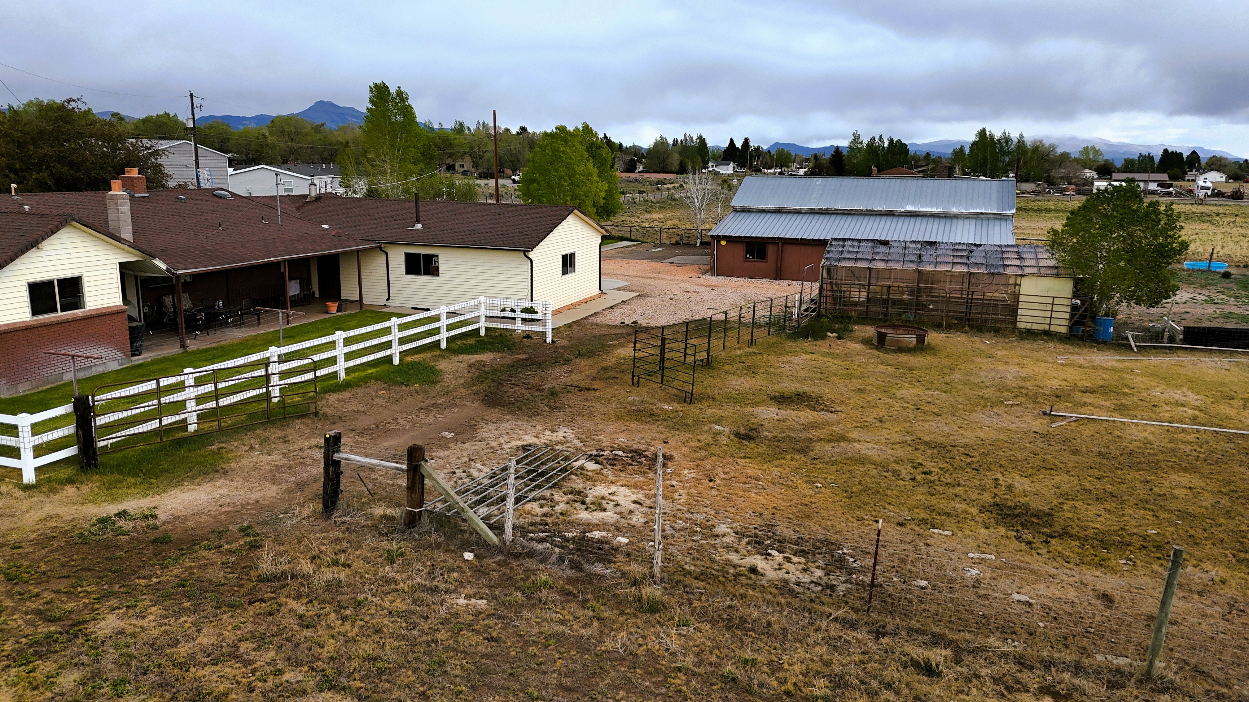 Expansive property featuring a single-story residence with a covered patio, a separate outbuilding with a metal roof, and a fenced enclosure
