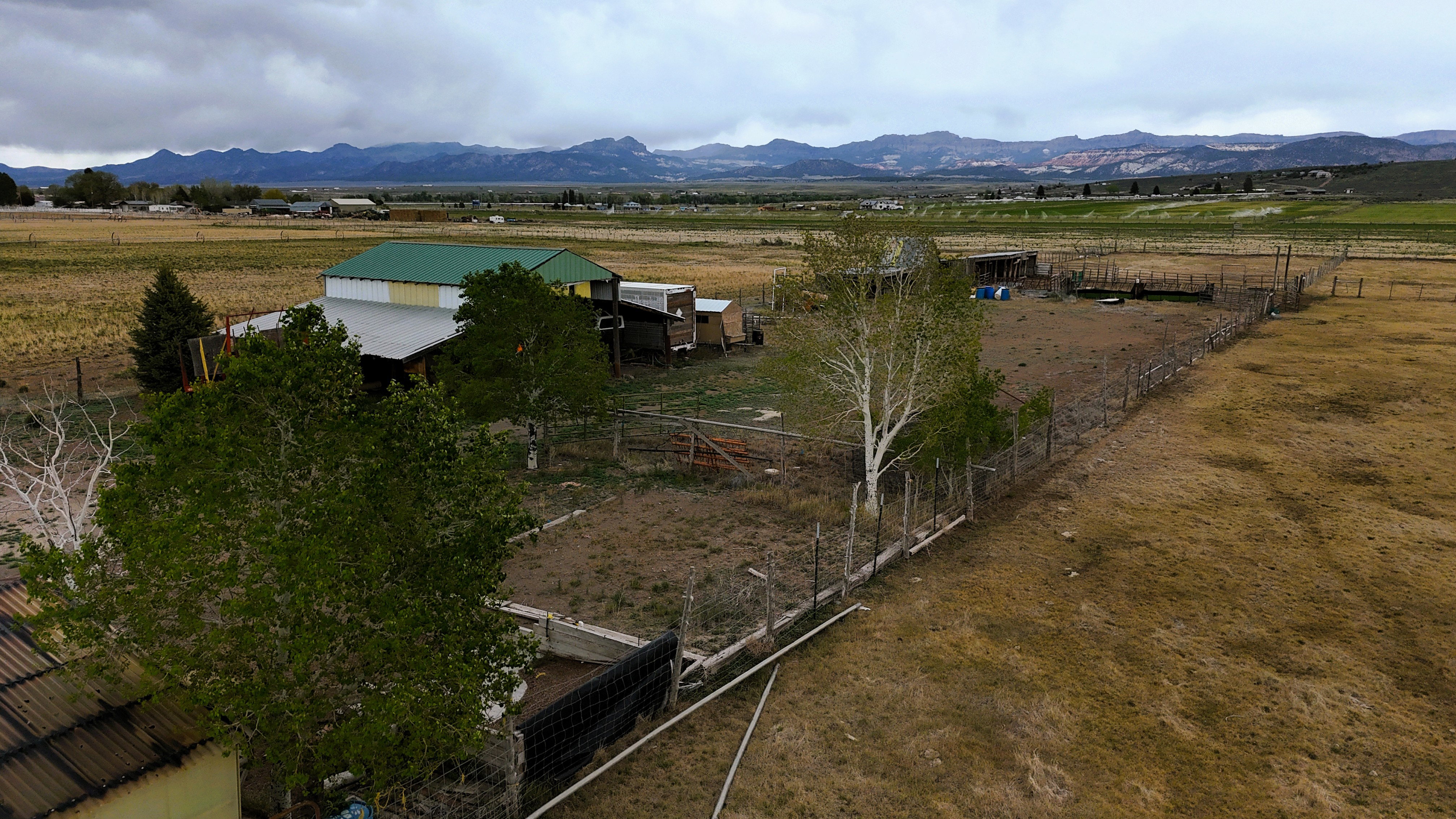 Expansive rural property featuring multiple outbuildings, fenced enclosures, mature trees, and mountainous terrain