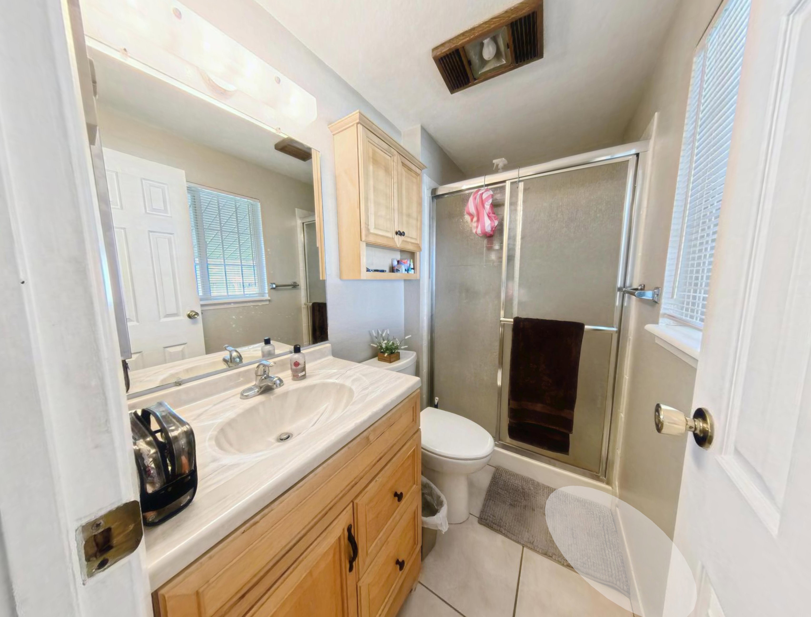 Bathroom featuring a single vanity with wood-finish cabinetry, a large mirror, and a shower with a sliding glass door enclosure