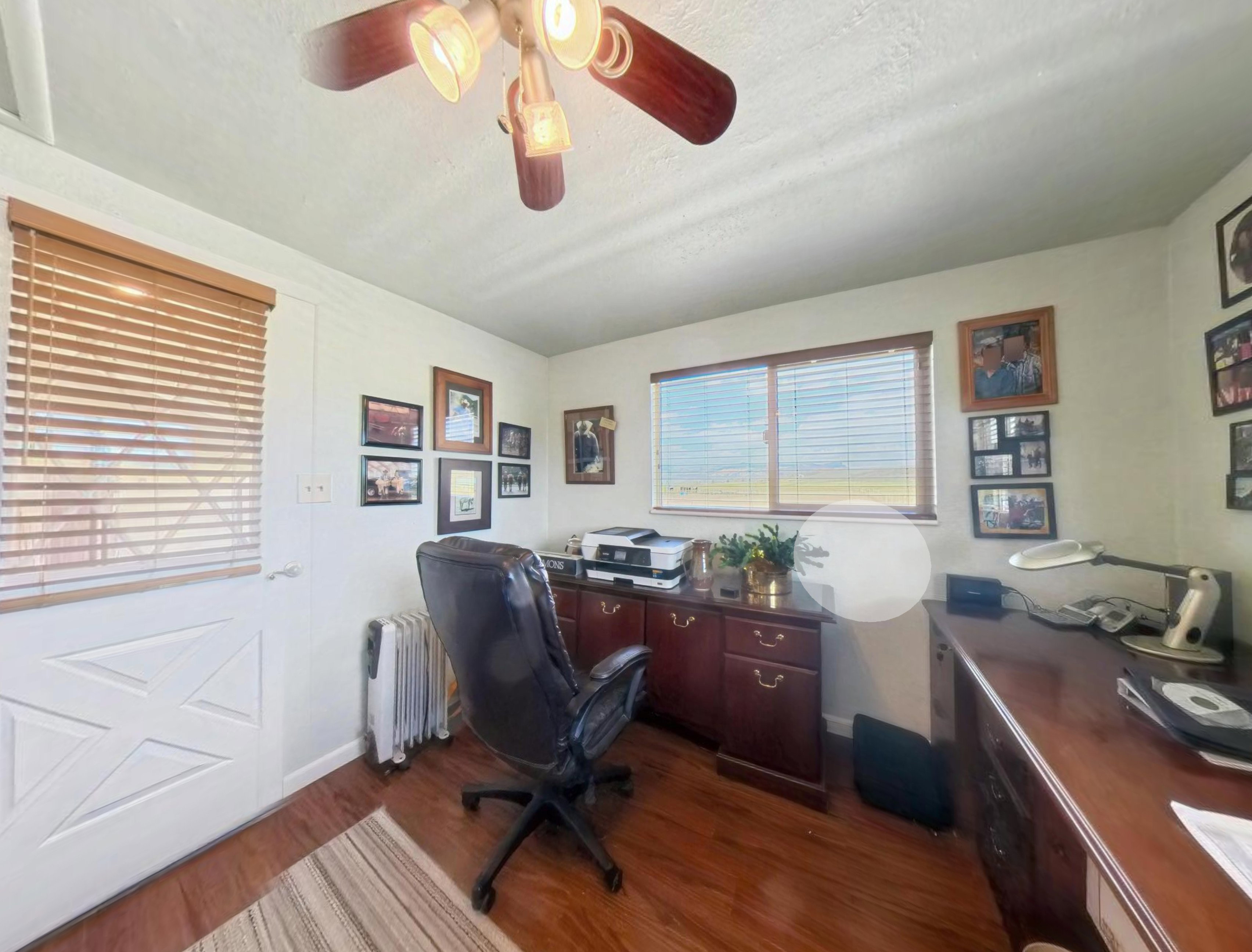 Room featuring wood-finish flooring, a ceiling fan with integrated lighting, and two windows with wood-tone blinds