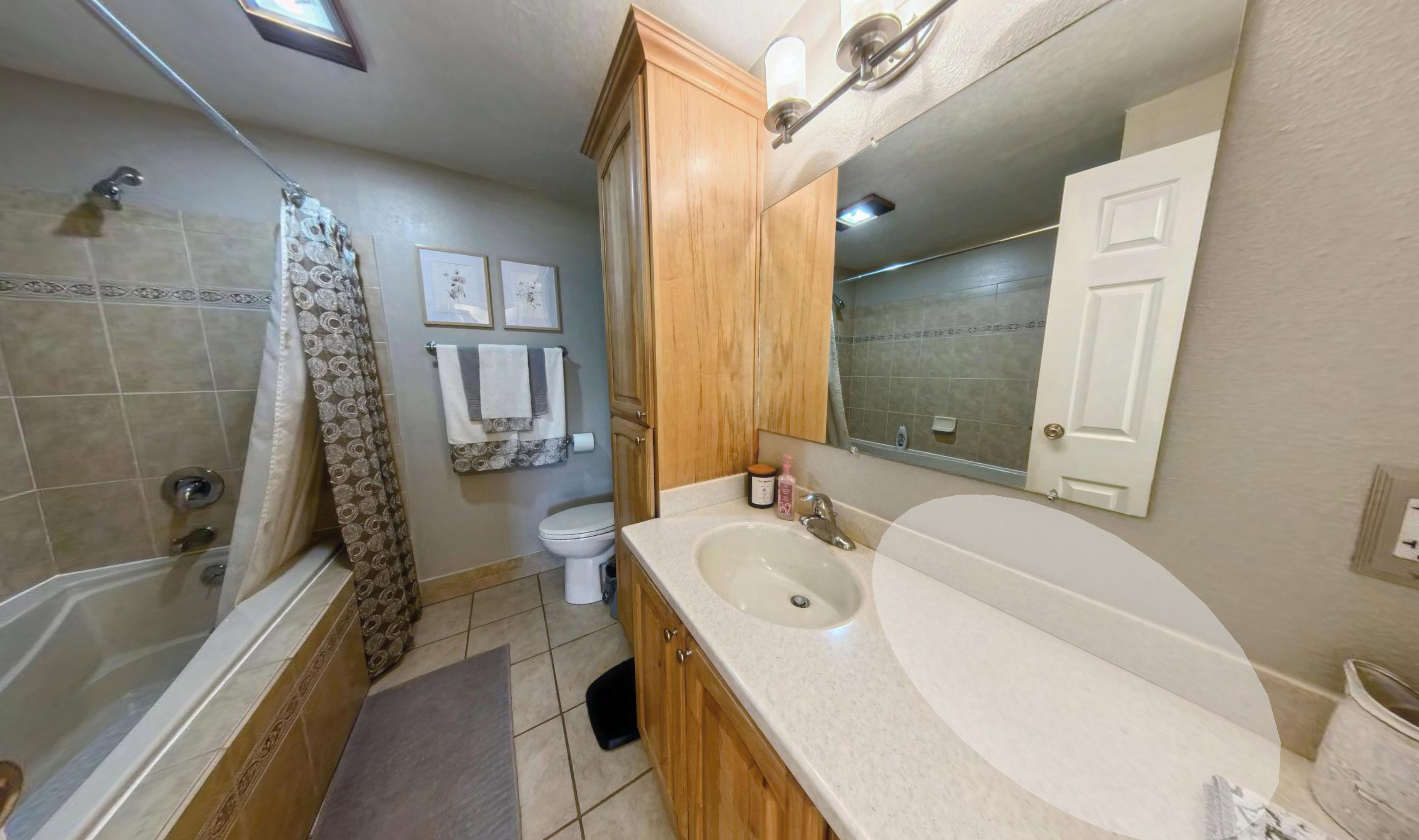 Bathroom featuring a built-in tub with tile surround, a single vanity with an integrated sink and light countertop, natural wood-finish cabinetry, and a full-width mirror
