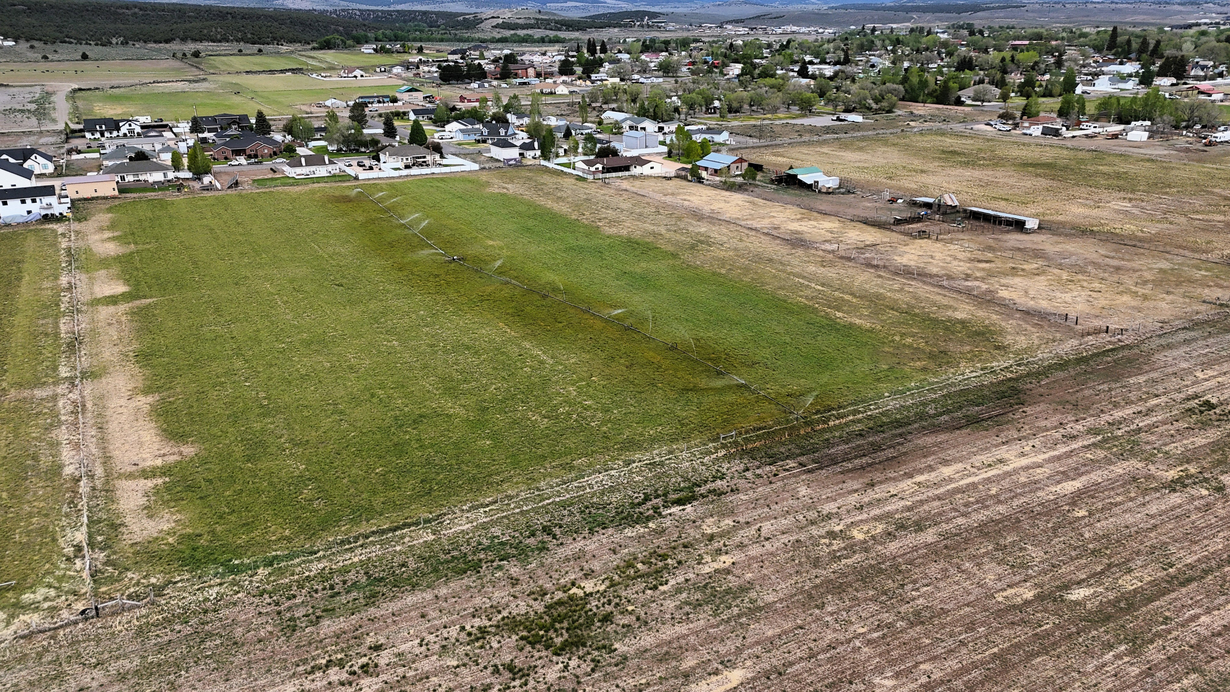 Expansive agricultural land featuring a partially tilled field, an irrigated green field, and distant structures