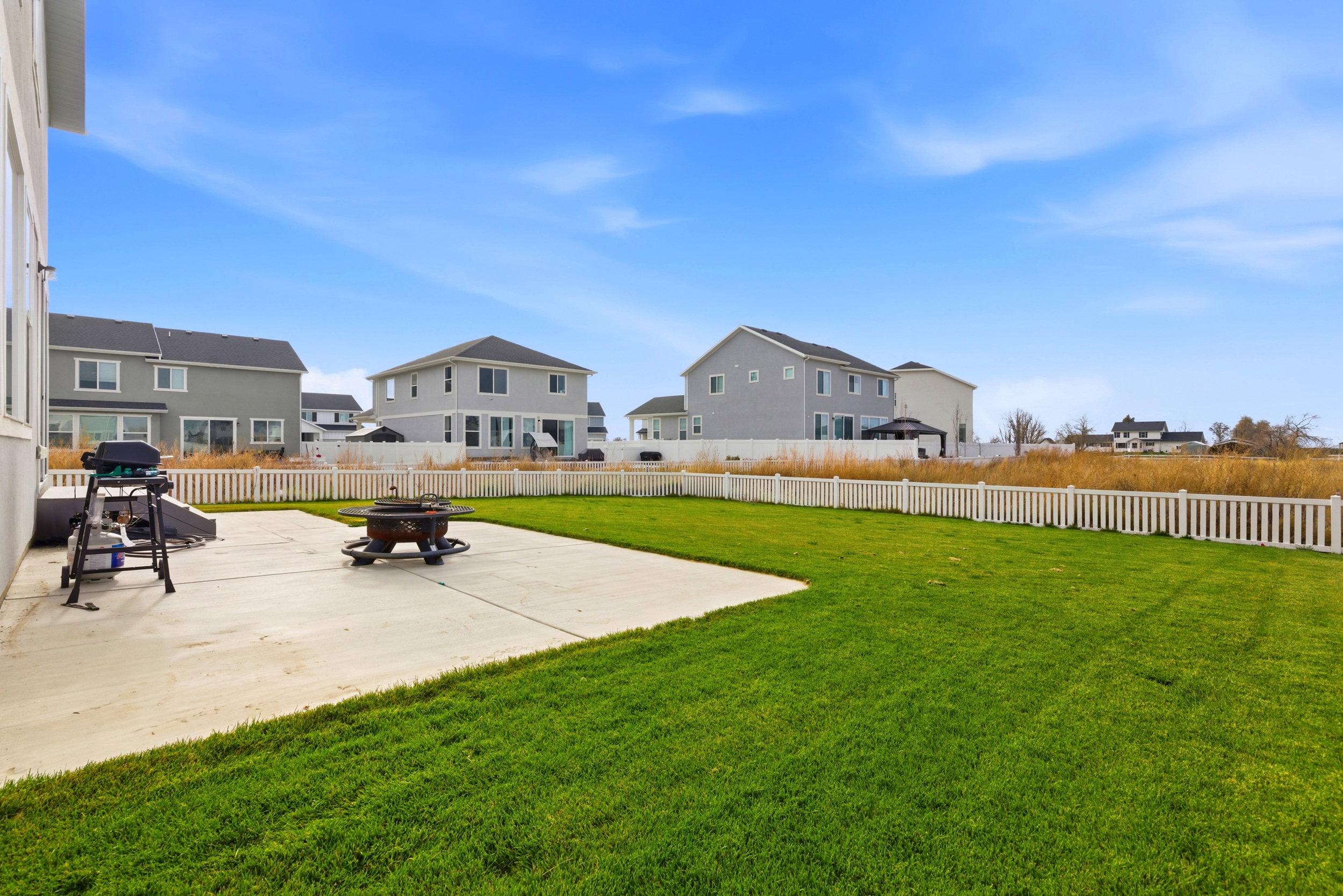 Expansive backyard featuring a large concrete patio, manicured lawn, and white picket fencing