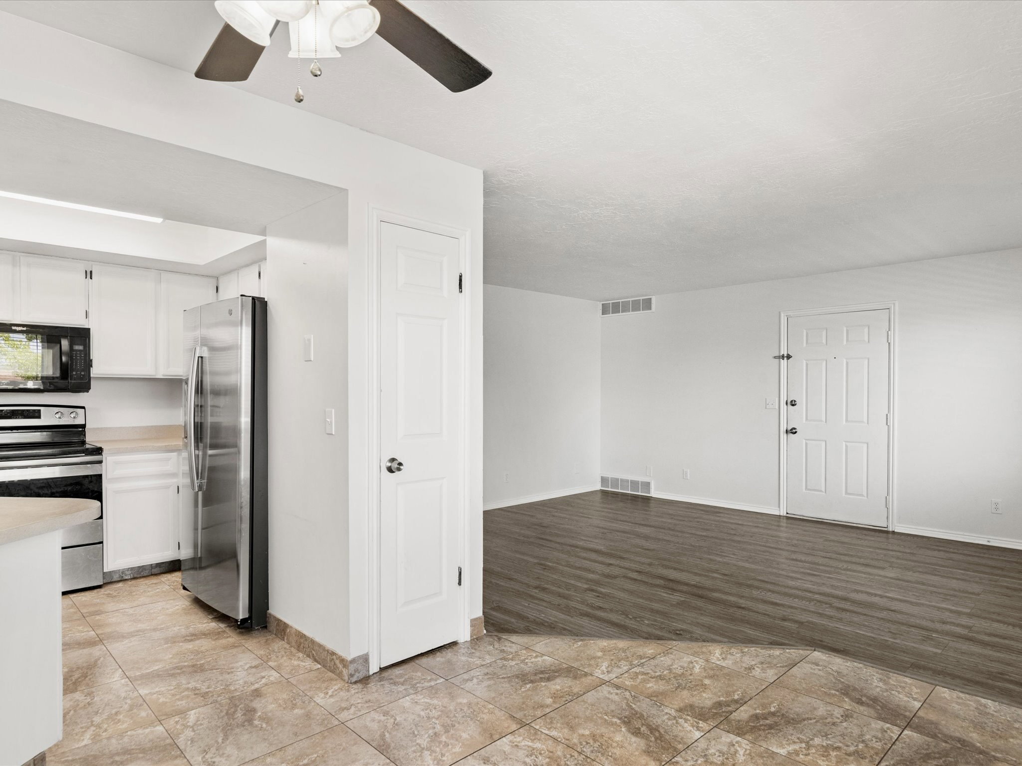 Kitchen and living area featuring a ceiling fan, wood-finish flooring, white paneled doors, and stainless steel appliances