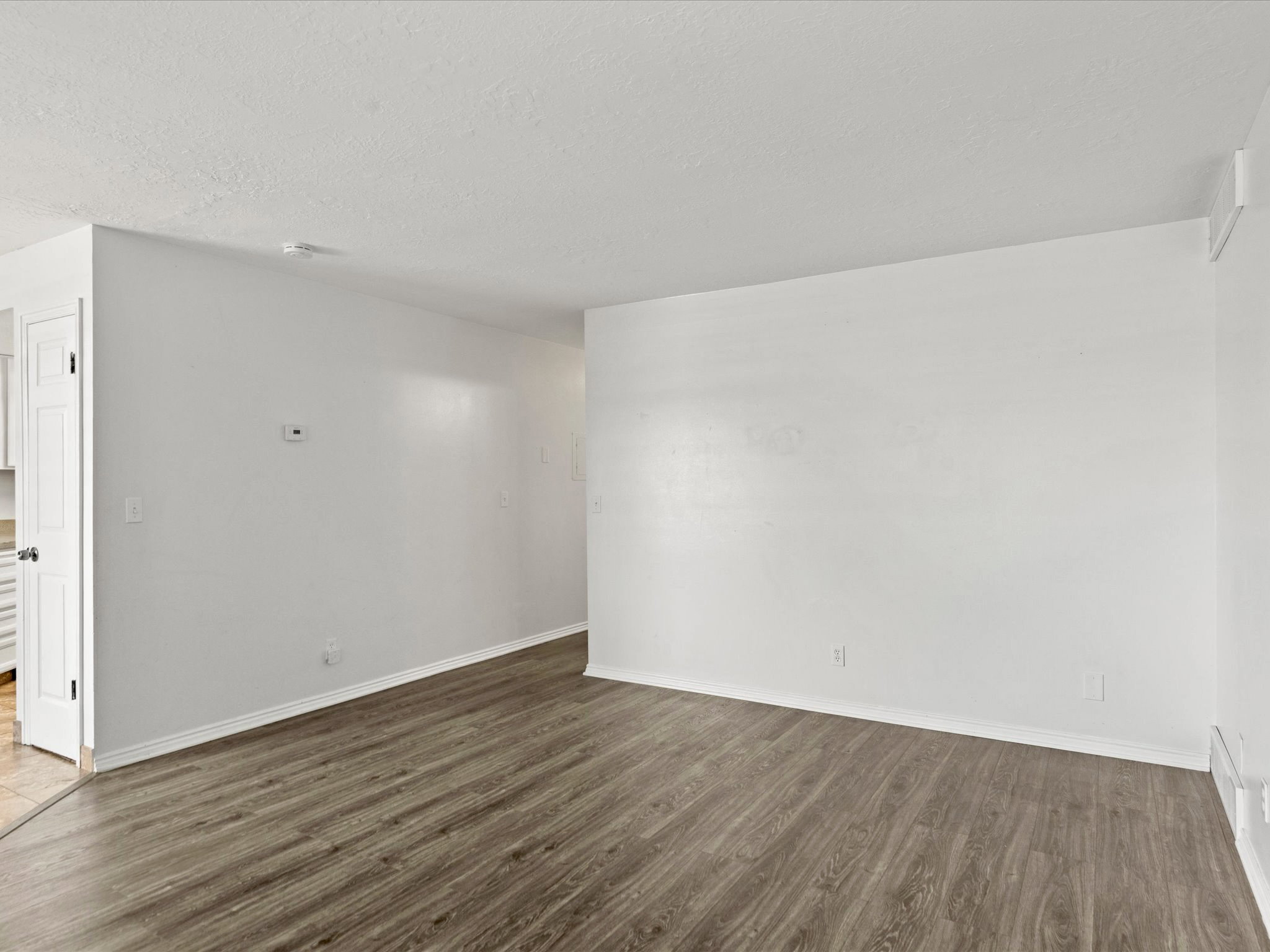 Spacious room featuring wood-finish flooring, white baseboards, and white walls