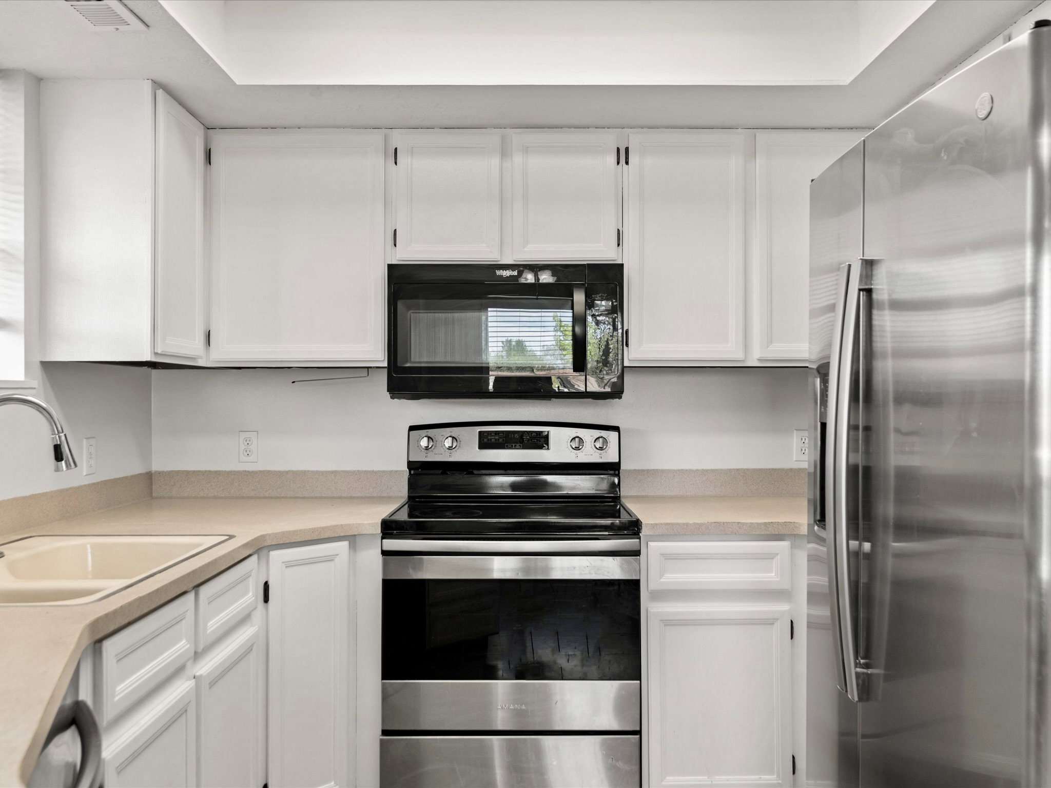 Kitchen featuring white cabinetry, light-toned countertops, stainless steel appliances, a corner sink with a gooseneck faucet, and an overhead microwave