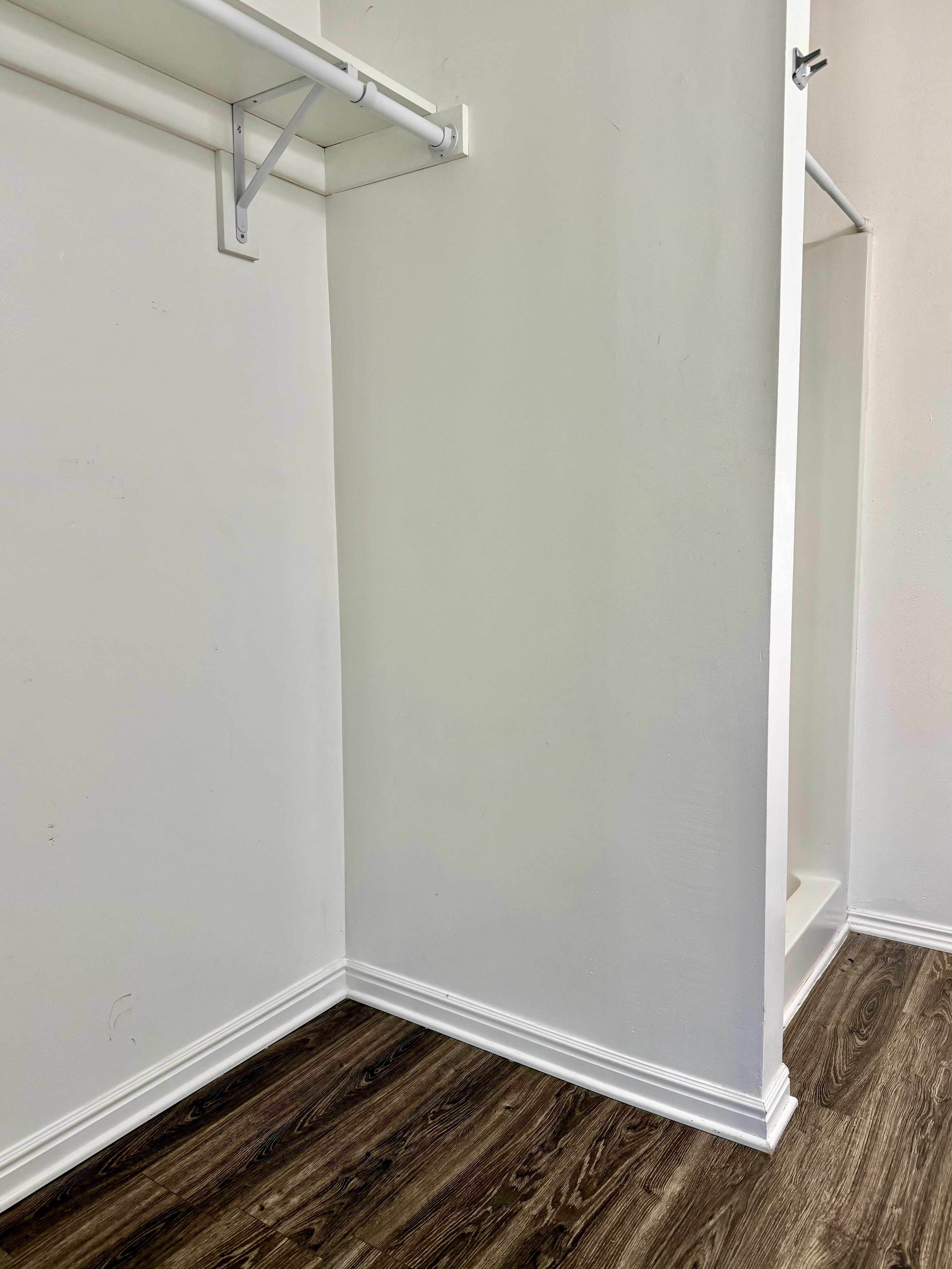 Walk-in closet featuring wood-finish flooring, white baseboards, and built-in shelving with hanging rods