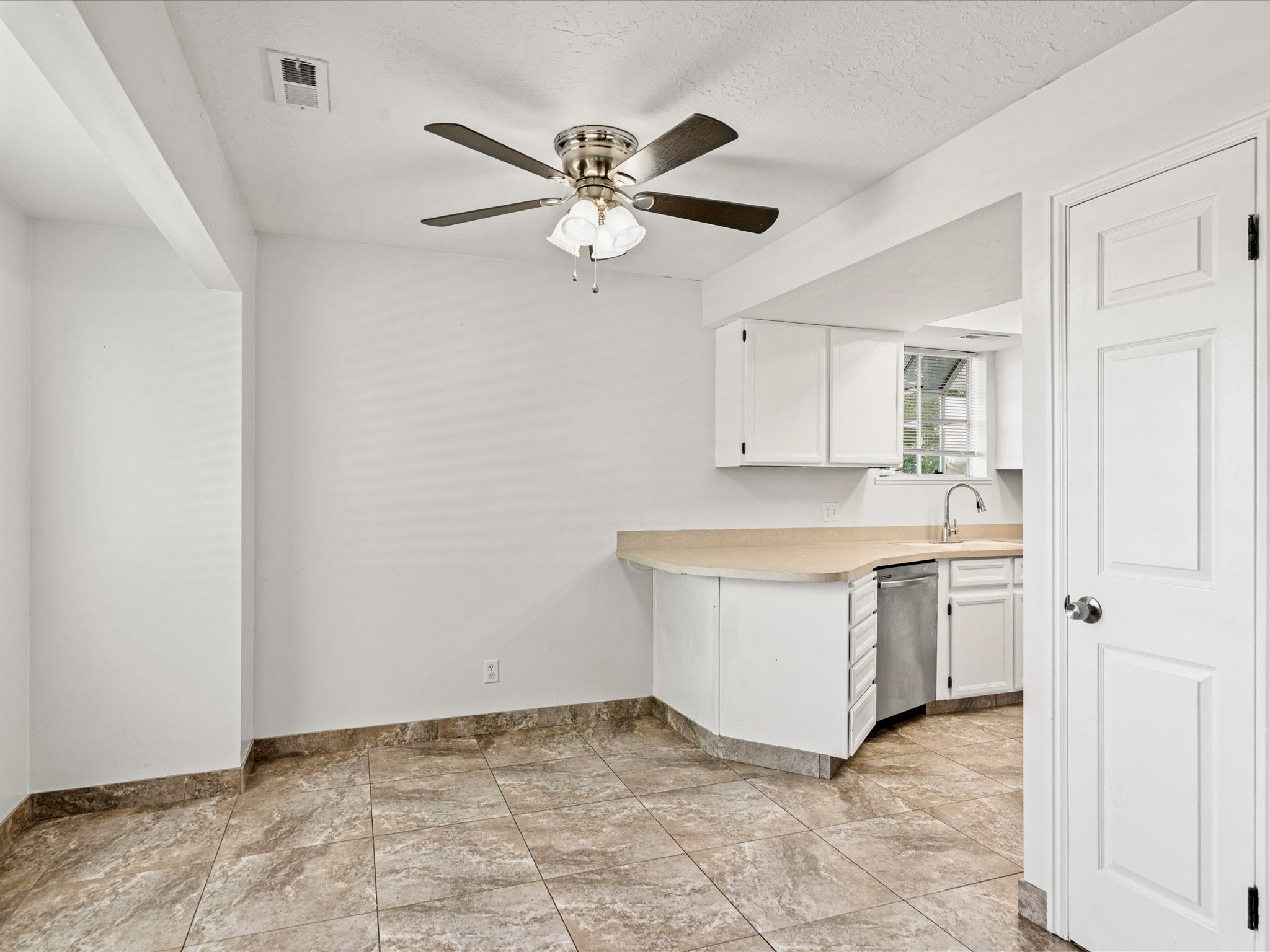 Kitchen area featuring a stainless steel dishwasher, white cabinetry, and a light-toned countertop
