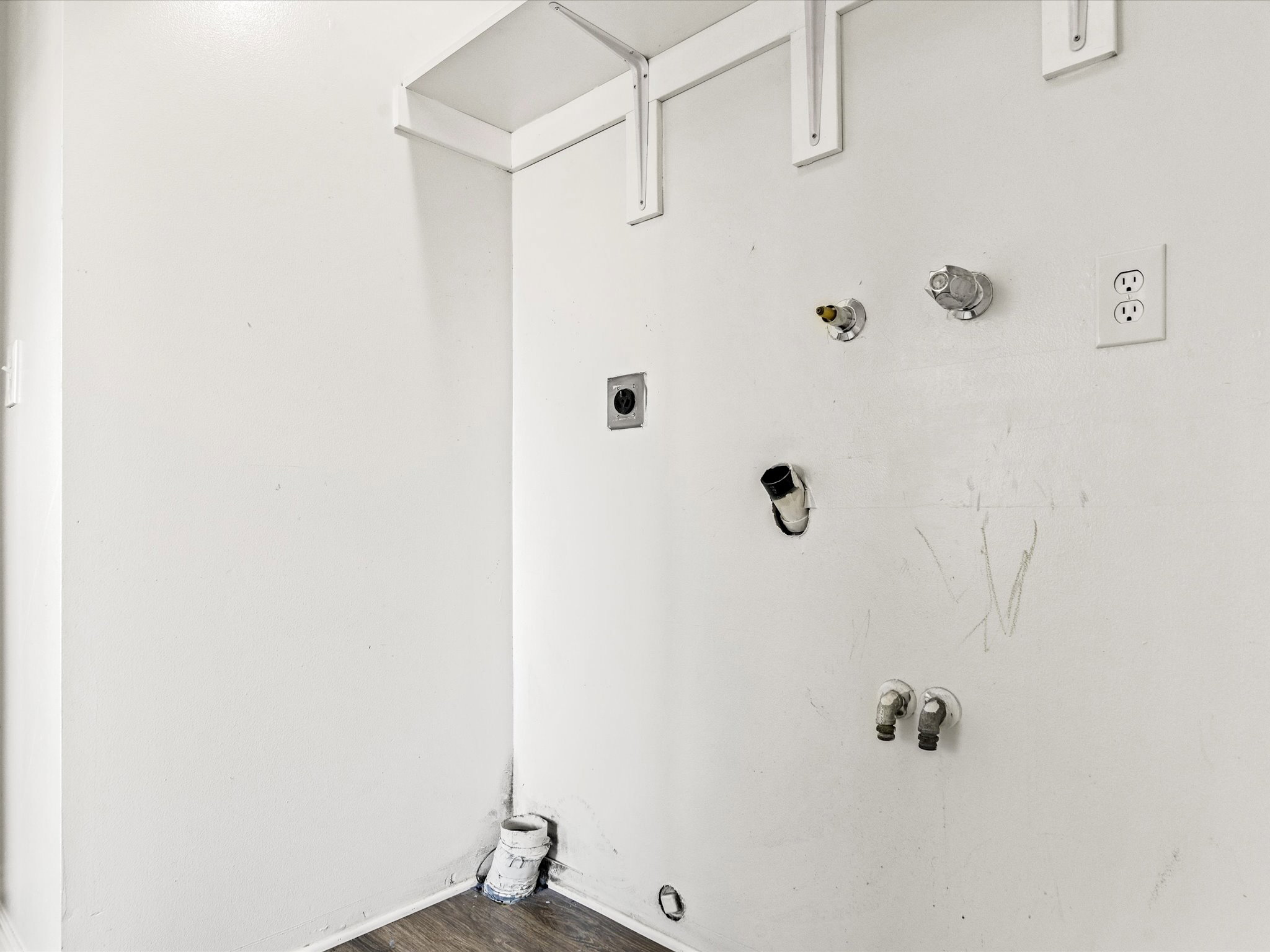 Dedicated laundry area featuring white walls, wood-finish flooring, and plumbing connections for appliances