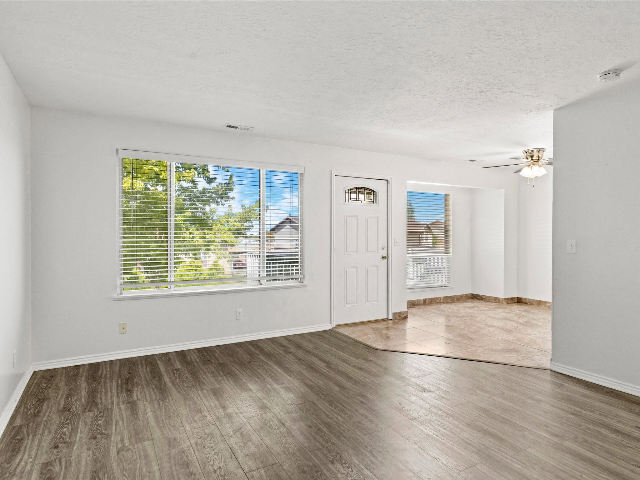 Entry room featuring wood-finish flooring, a white front door with an arched window insert, and a large window with blinds
