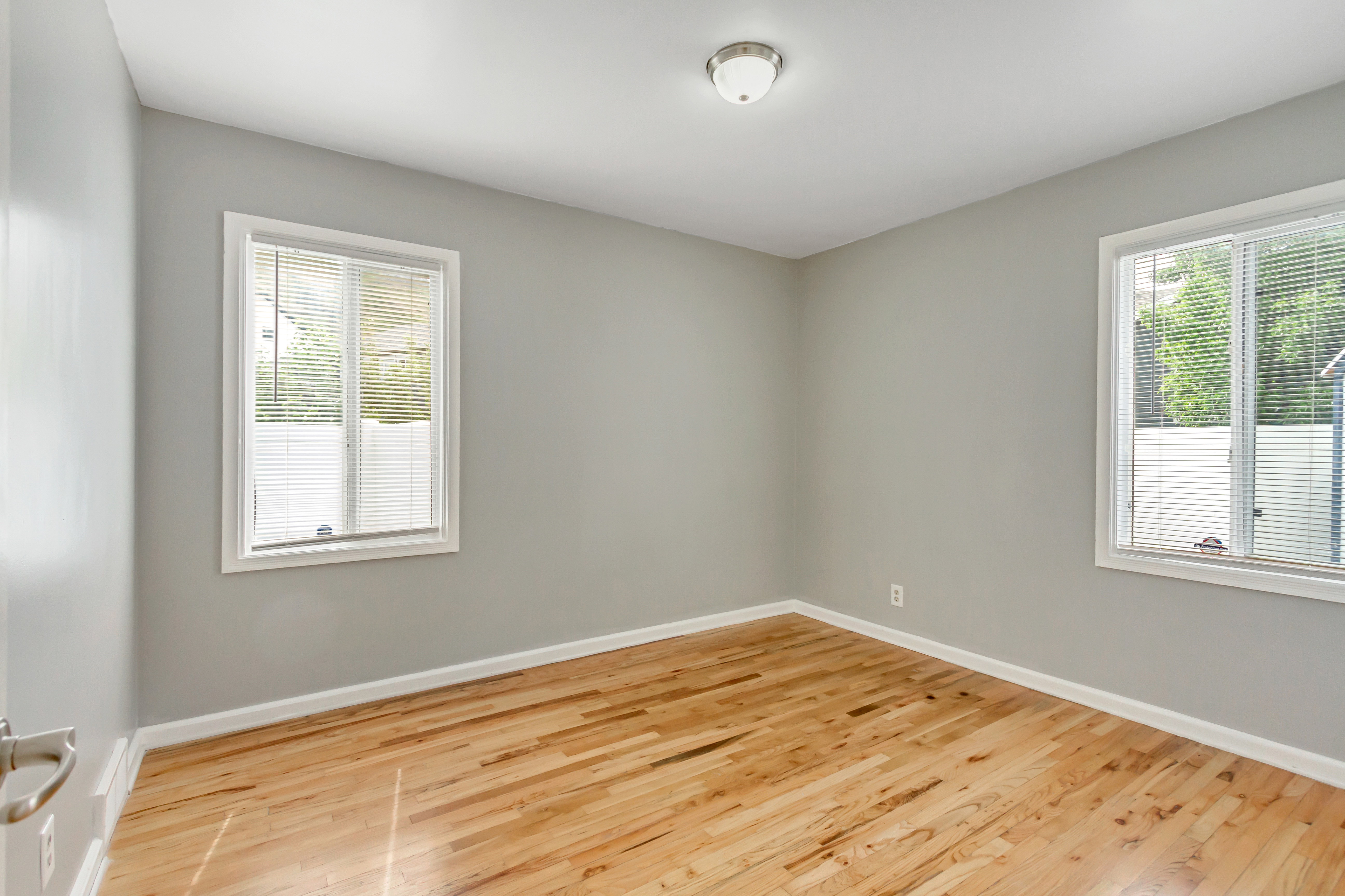 Bright room featuring two windows with white blinds, wood-finish flooring, light gray wall paint, and white baseboards