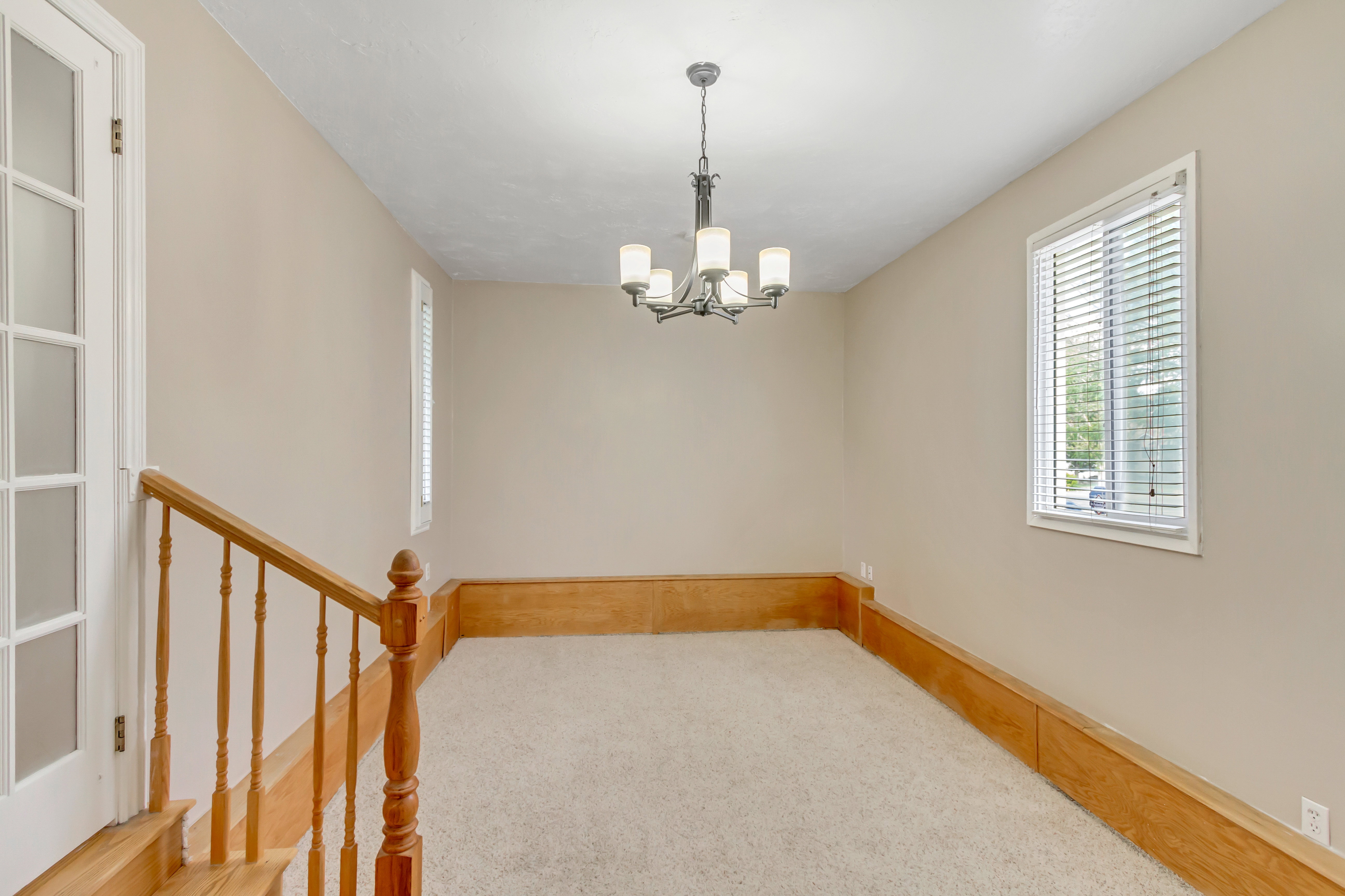 Carpeted room featuring a ceiling-mounted chandelier, natural wood trim, white window blinds, and a white French door with frosted glass panels
