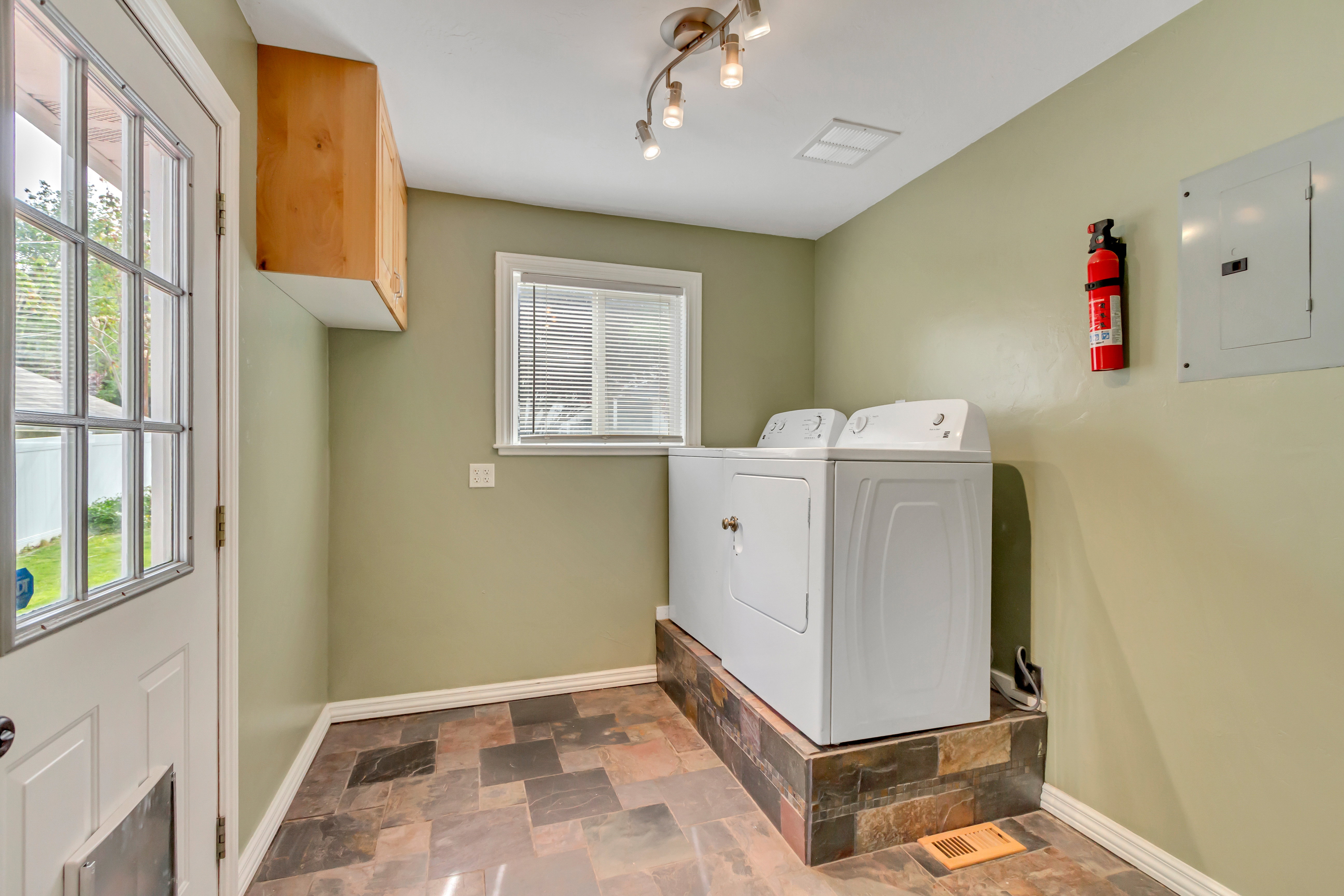 Dedicated laundry area featuring a raised platform, wood-finish overhead cabinetry, and multi-toned floor tiling