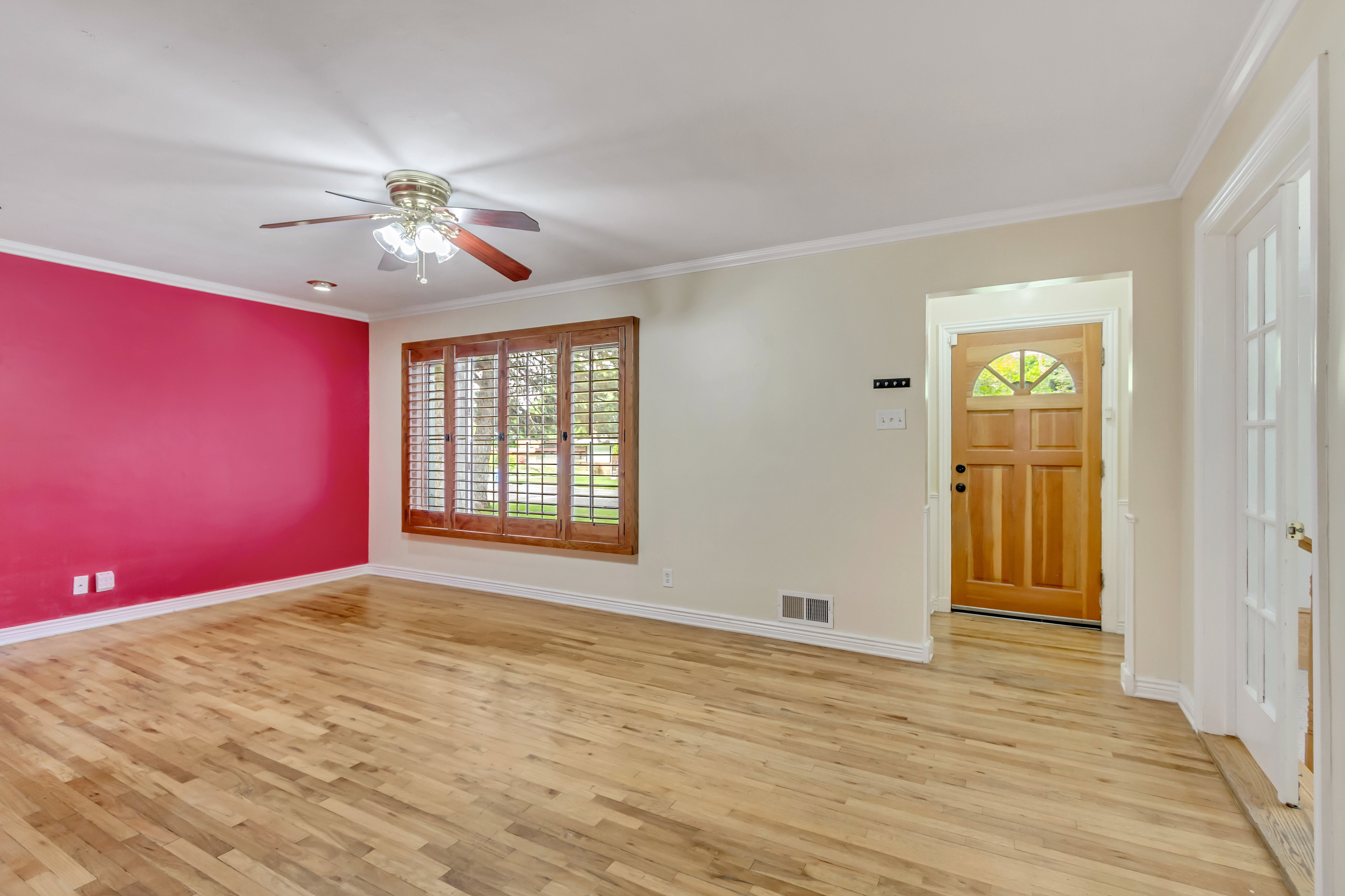 Hardwood flooring throughout featuring crown molding, a ceiling fan with integrated lighting, and a front entry door with an arched glass insert