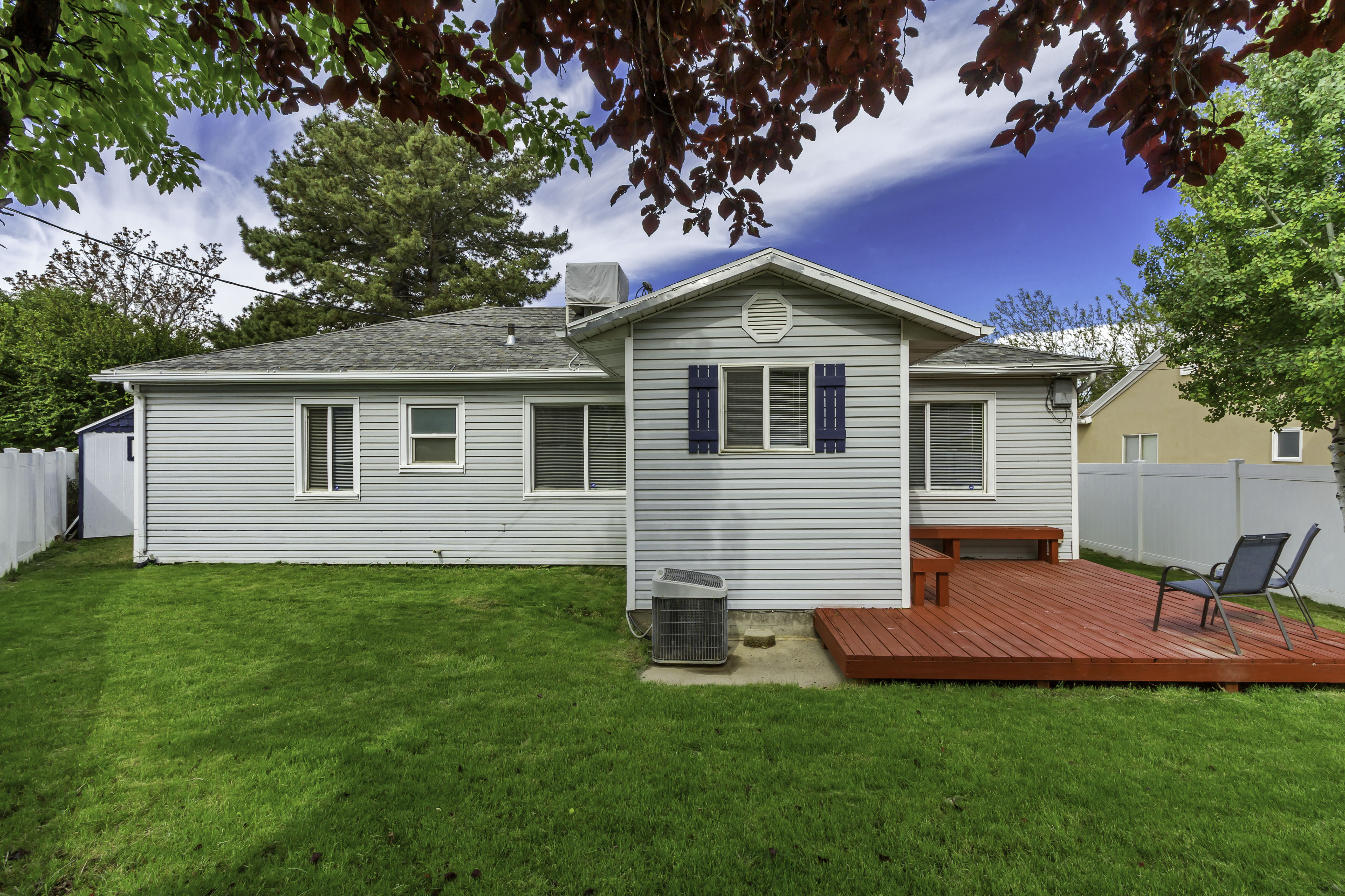 Rear exterior featuring light gray siding, a vibrant red wood-plank deck with built-in seating, and a lush green lawn
