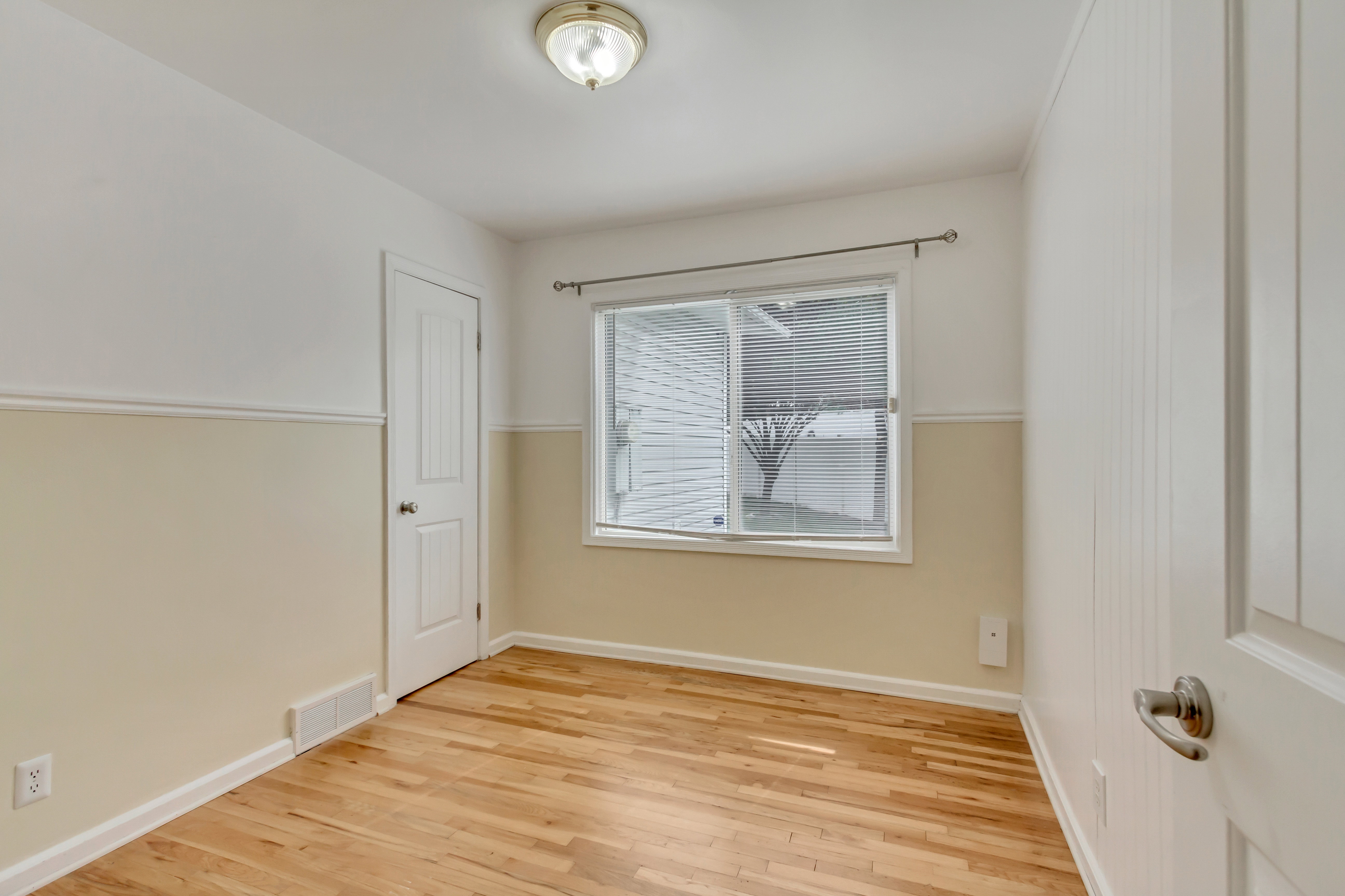 Hardwood flooring, painted wainscoting, white baseboards, and a contemporary ceiling light fixture
