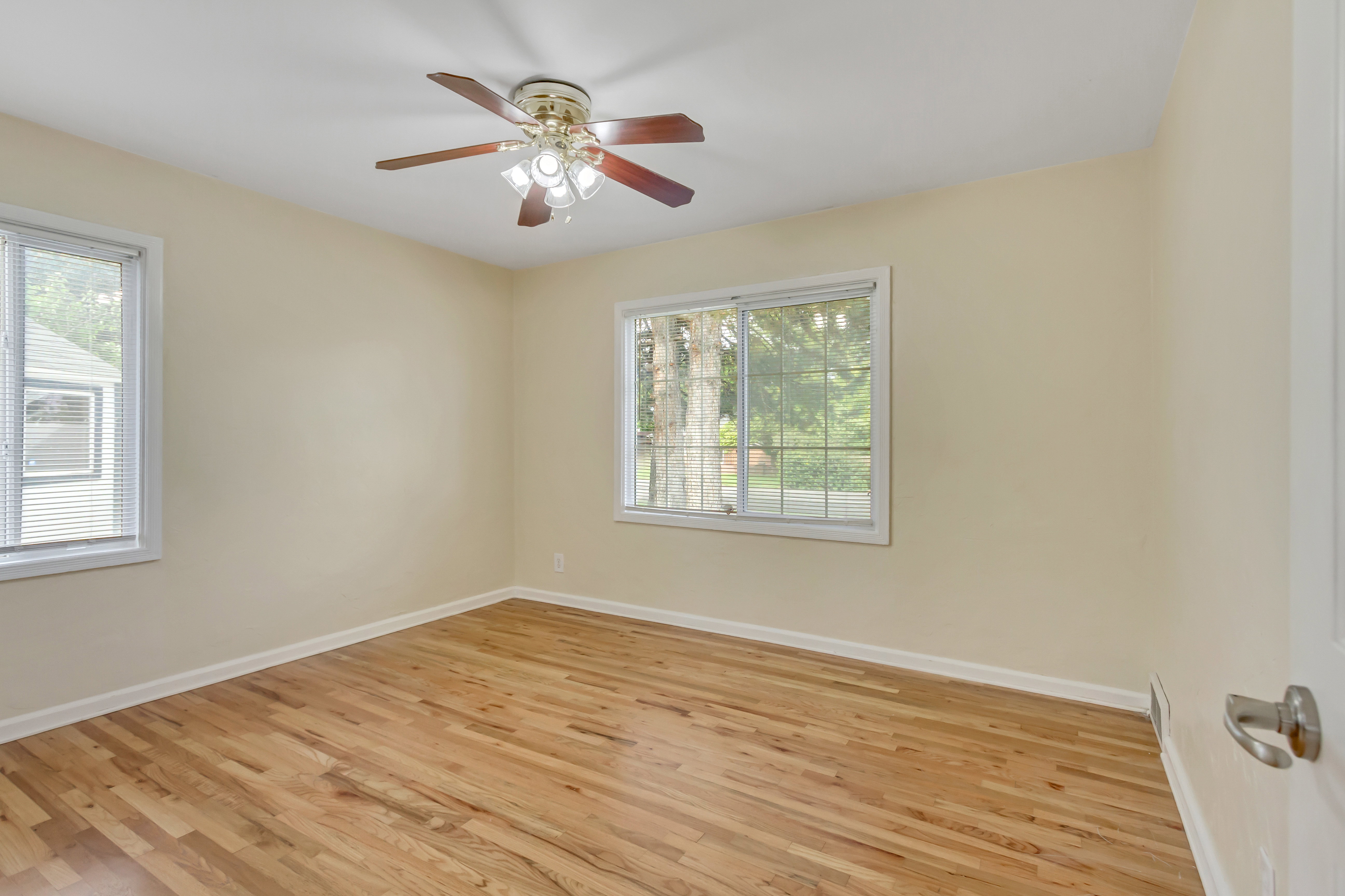 Room featuring wood-finish flooring, two windows, a ceiling fan with integrated lighting, and neutral wall paint