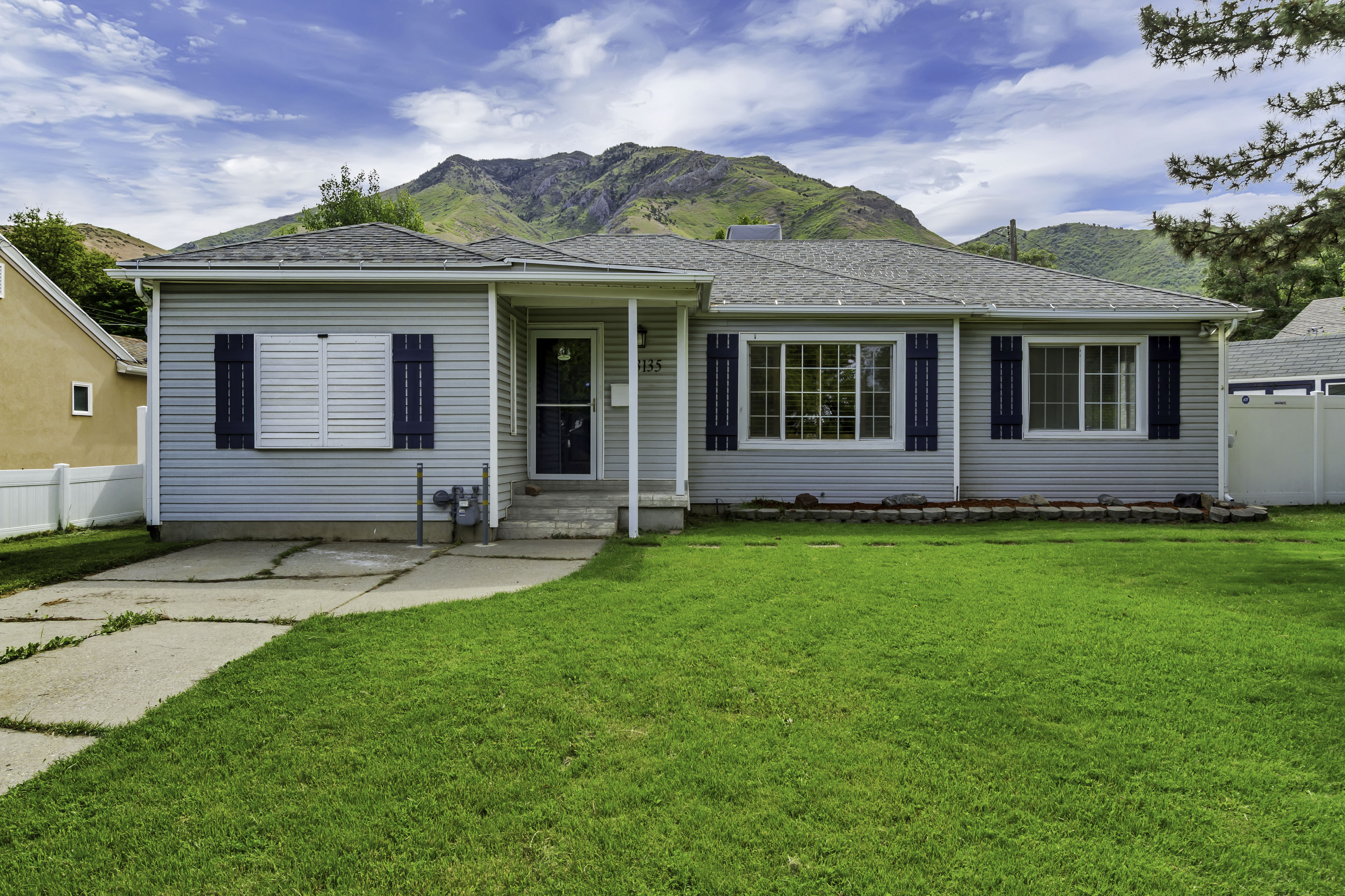 Ranch-style exterior with light blue siding, a covered porch entry, and a prominent mountain backdrop