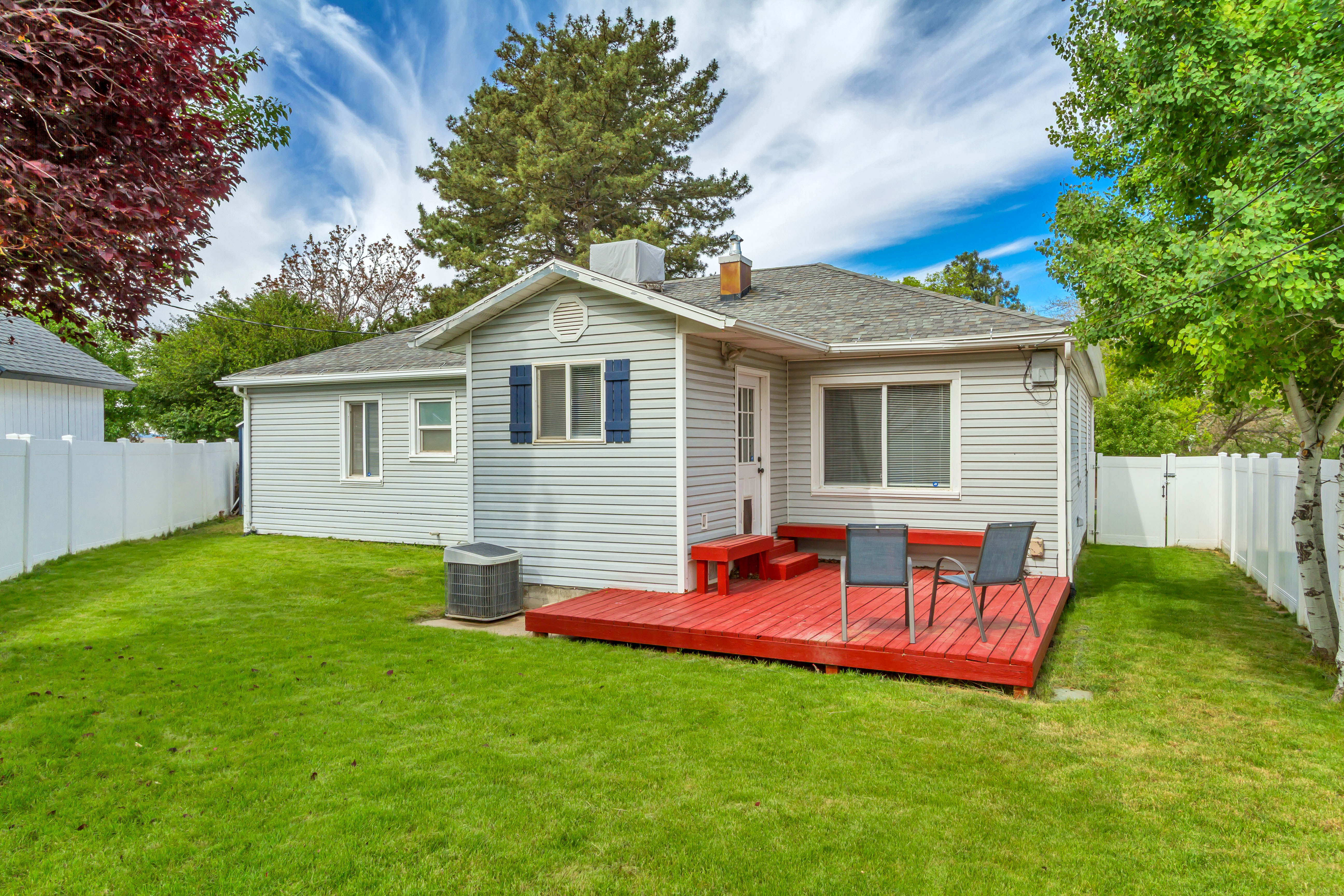 Rear exterior featuring a vibrant red deck, light grey siding, and a white vinyl privacy fence