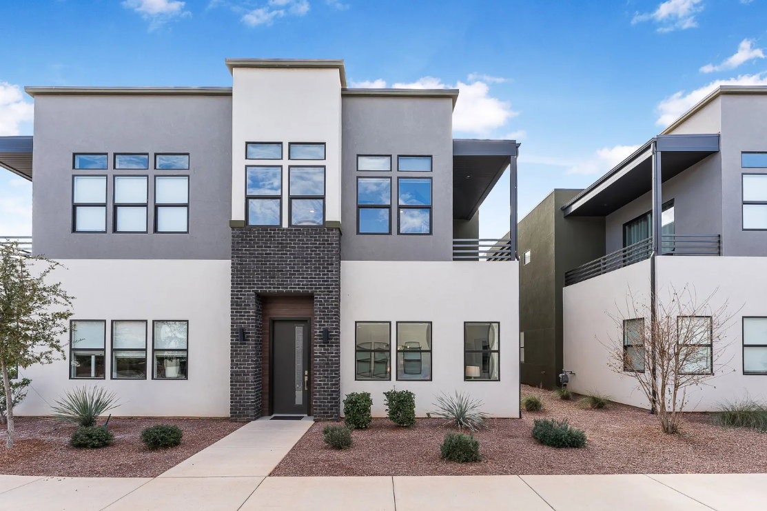 Modern multi-story facade featuring a dark brick entry column, a dark entry door with frosted glass panel, and large black-framed windows