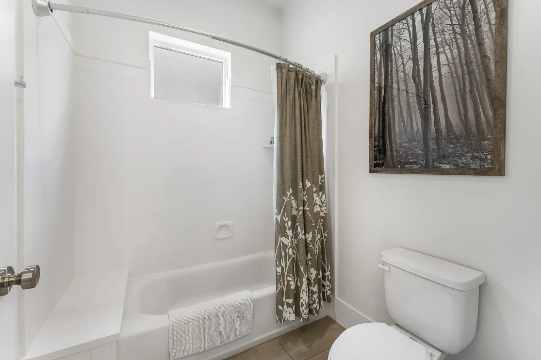Bathroom featuring a white bathtub, white toilet, and a window above the tub