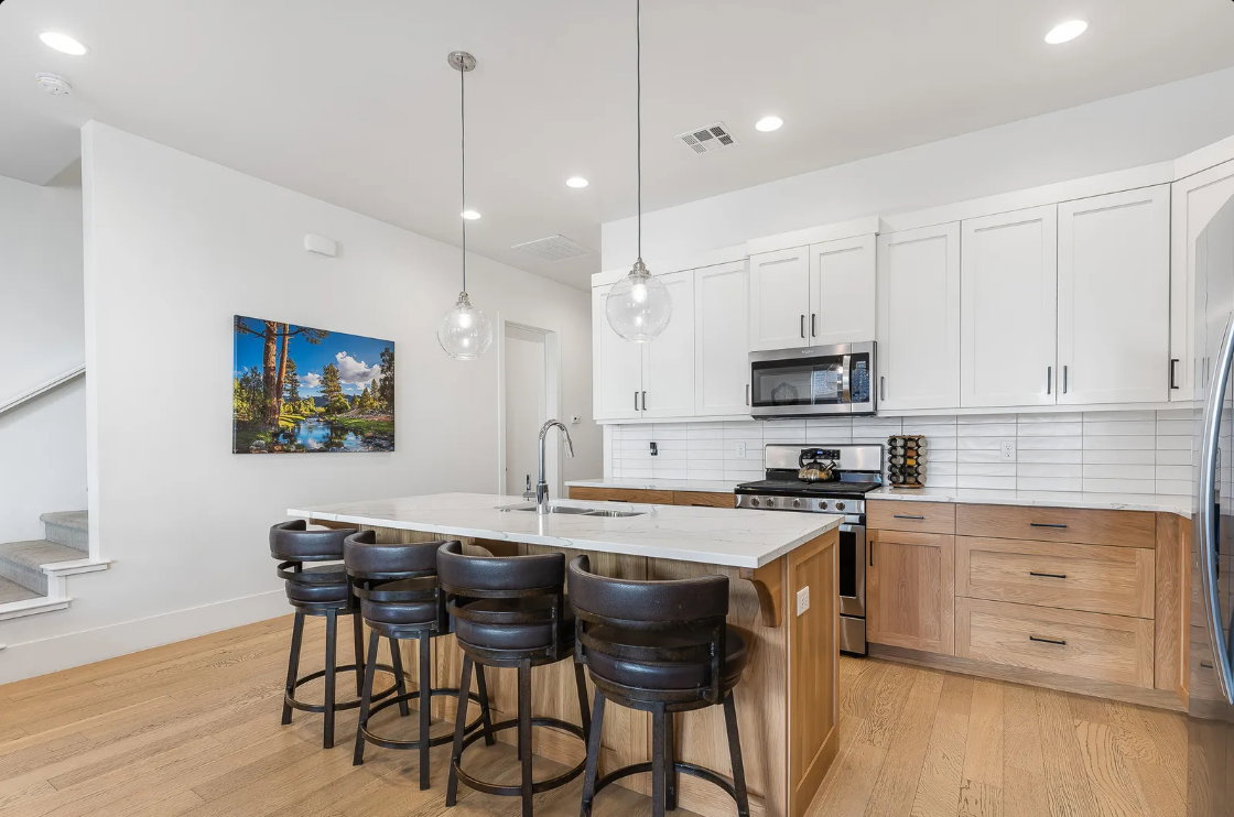 Contemporary kitchen featuring a large island with seating, white shaker upper cabinetry, light wood-finish lower cabinetry, subway tile backsplash, and stainless steel appliances
