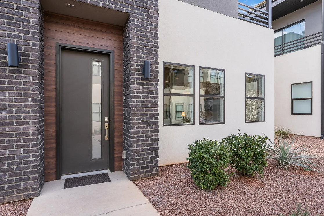 Contemporary exterior featuring dark brick accents, a wood-paneled entry, and a modern front door with a vertical window insert