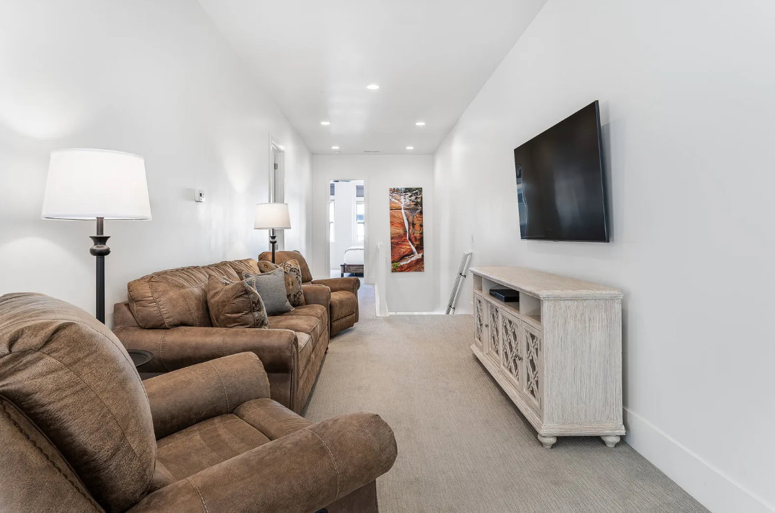 Spacious entertainment area featuring recessed lighting, light-colored carpeting, a wall-mounted television, and a decorative console cabinet