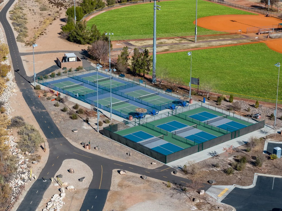 Multiple pickleball courts with perimeter fencing, illuminated by integrated lighting