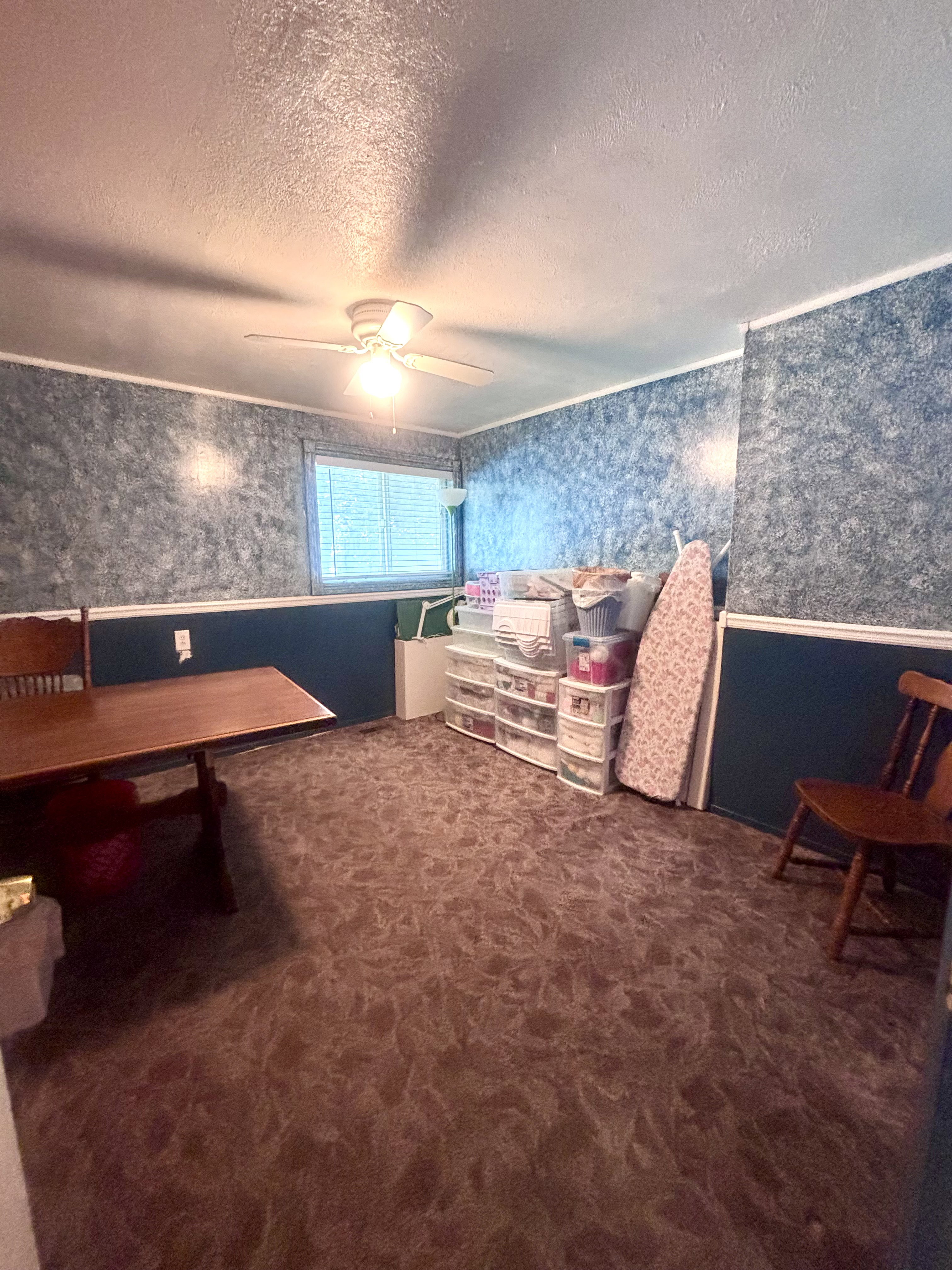 Room featuring patterned brown carpeting, dual-toned walls with a blue textured upper section and a darker solid lower section, and a ceiling fan with integrated lighting