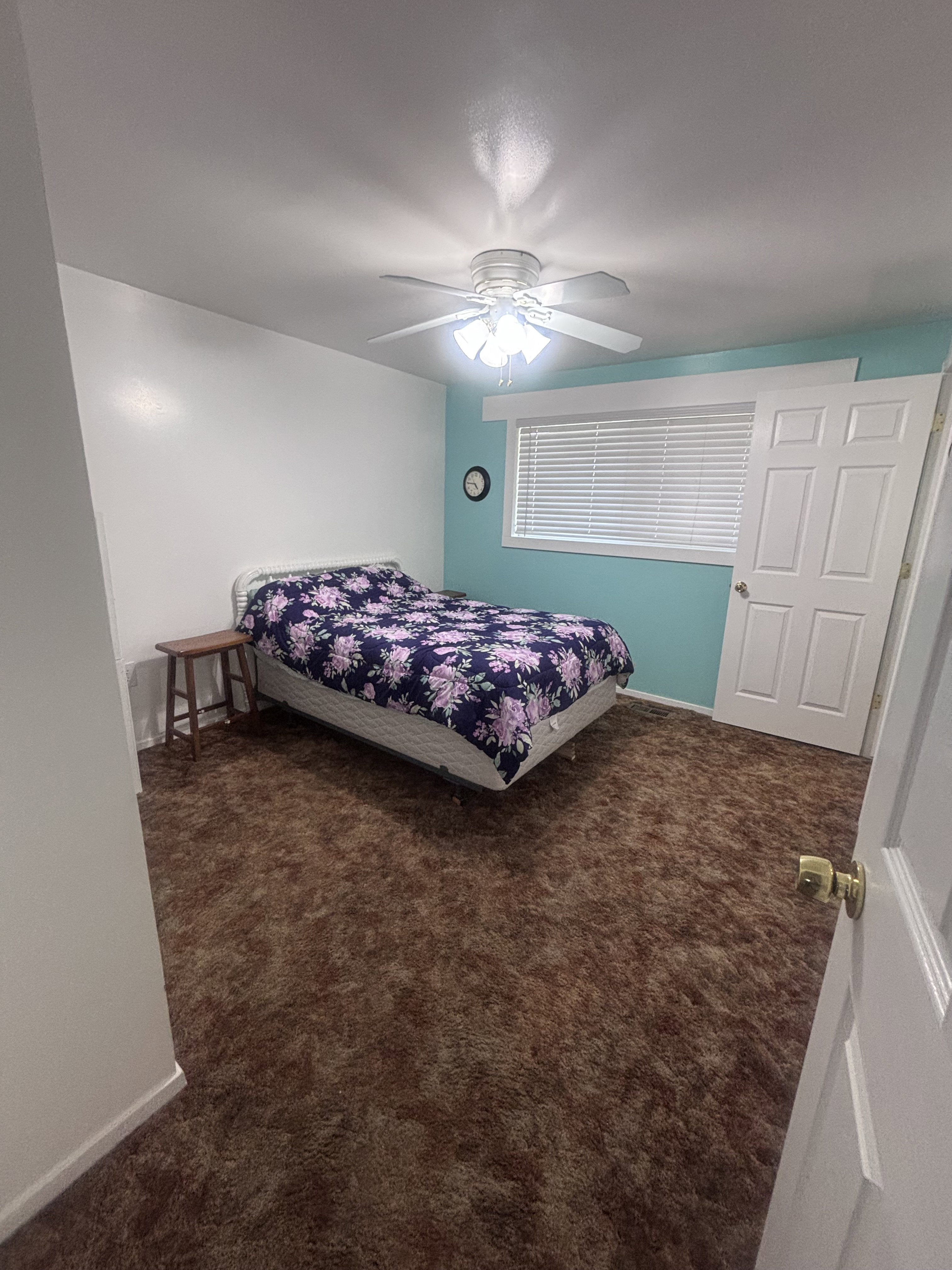 Bedroom featuring wall-to-wall brown carpeting, a white ceiling fan with integrated lighting, white interior doors, and a window with horizontal blinds